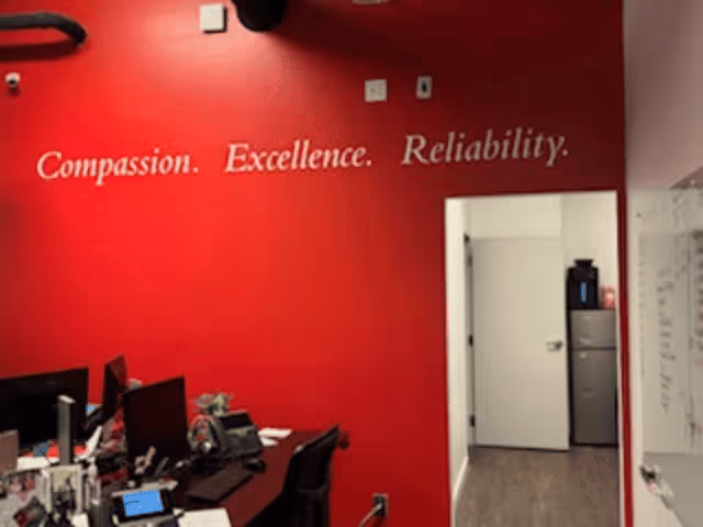 Red-walled reception area with desks, computers, and office supplies inside a senior care facility.