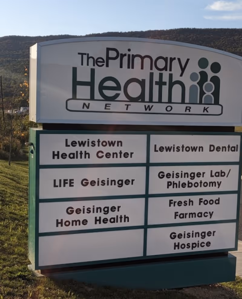 Outdoor sign for The Primary Health Network listing Lewistown Health Center and Geisinger services.