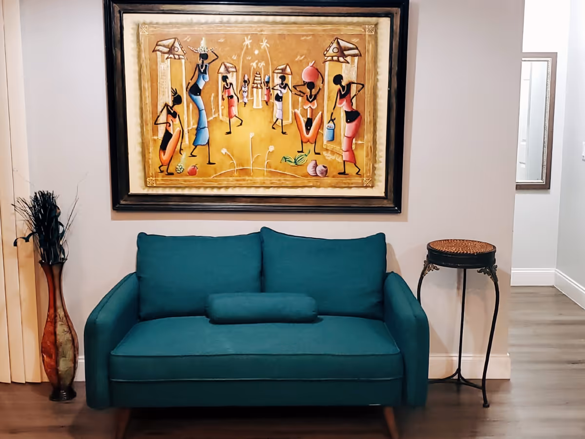 Teal sofa with a painting above, a tall vase, and a small side table.