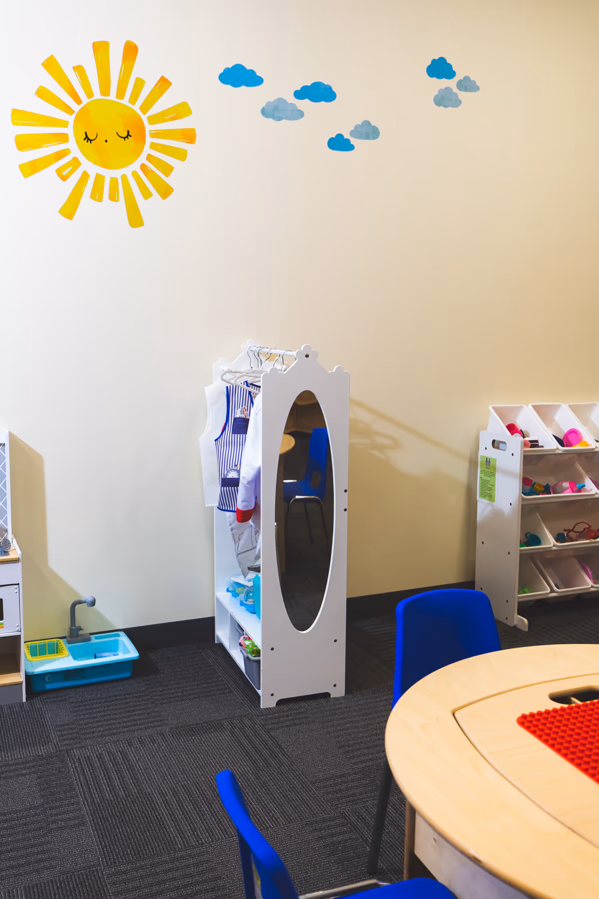 Interior playroom with blue chairs, mirror cabinet, toy shelves, and sun-wall art.