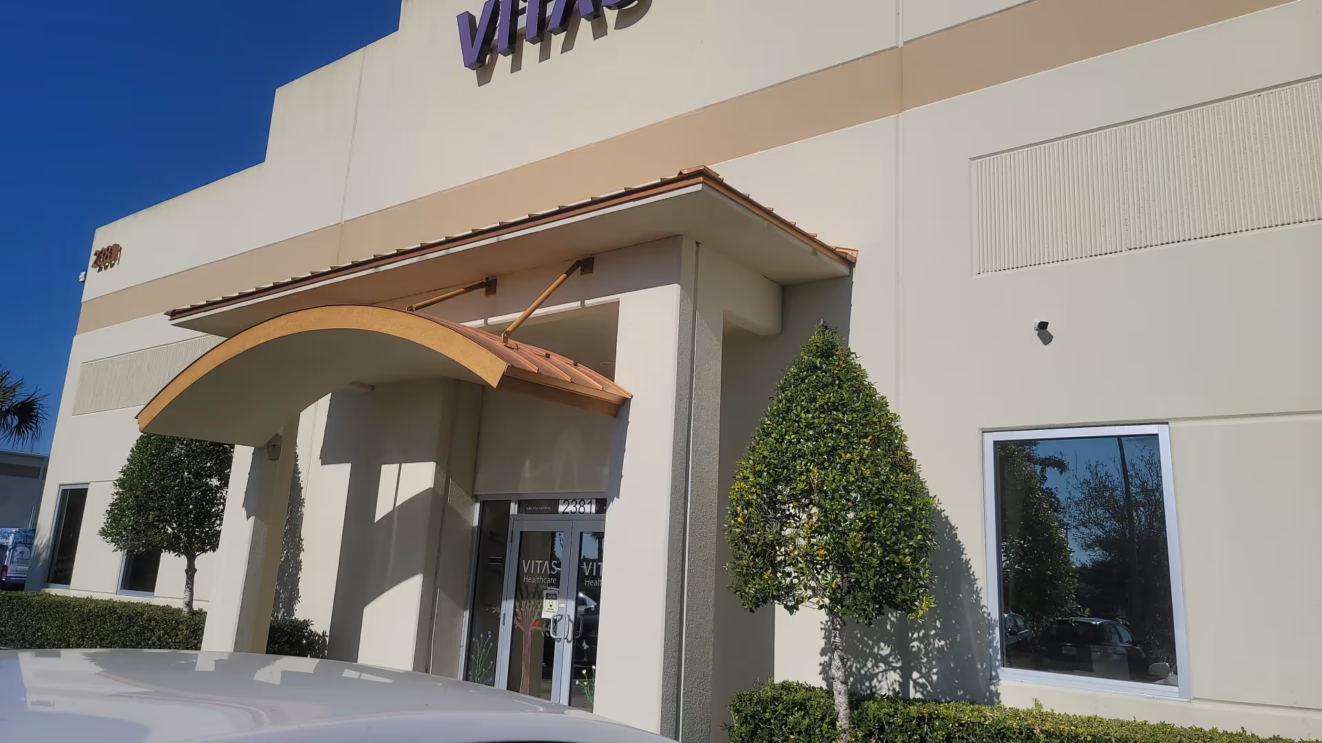 Exterior view of VITAS Healthcare building entrance with curved canopy and trimmed trees.