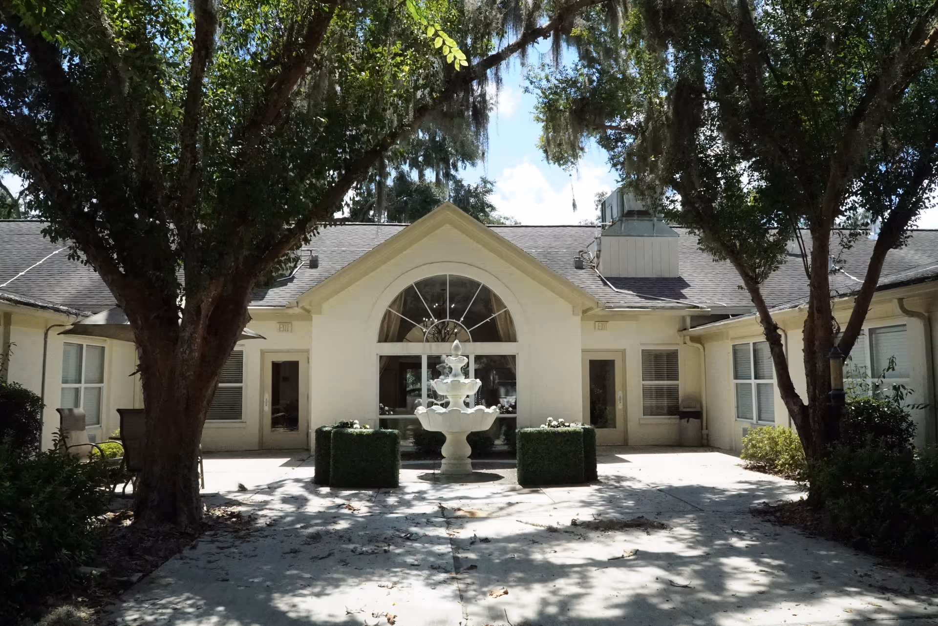 Front view of Palm Garden of Gainesville with arched window, fountain, and trees.