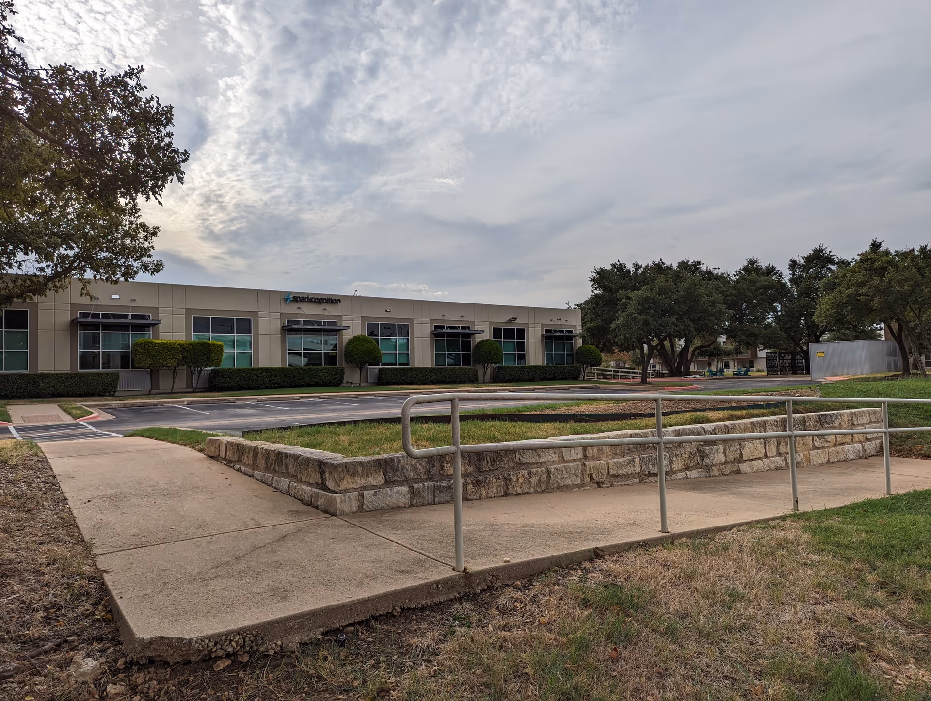 Exterior view of a single-story facility with ramp, trimmed hedges, trees, and a parking lot.