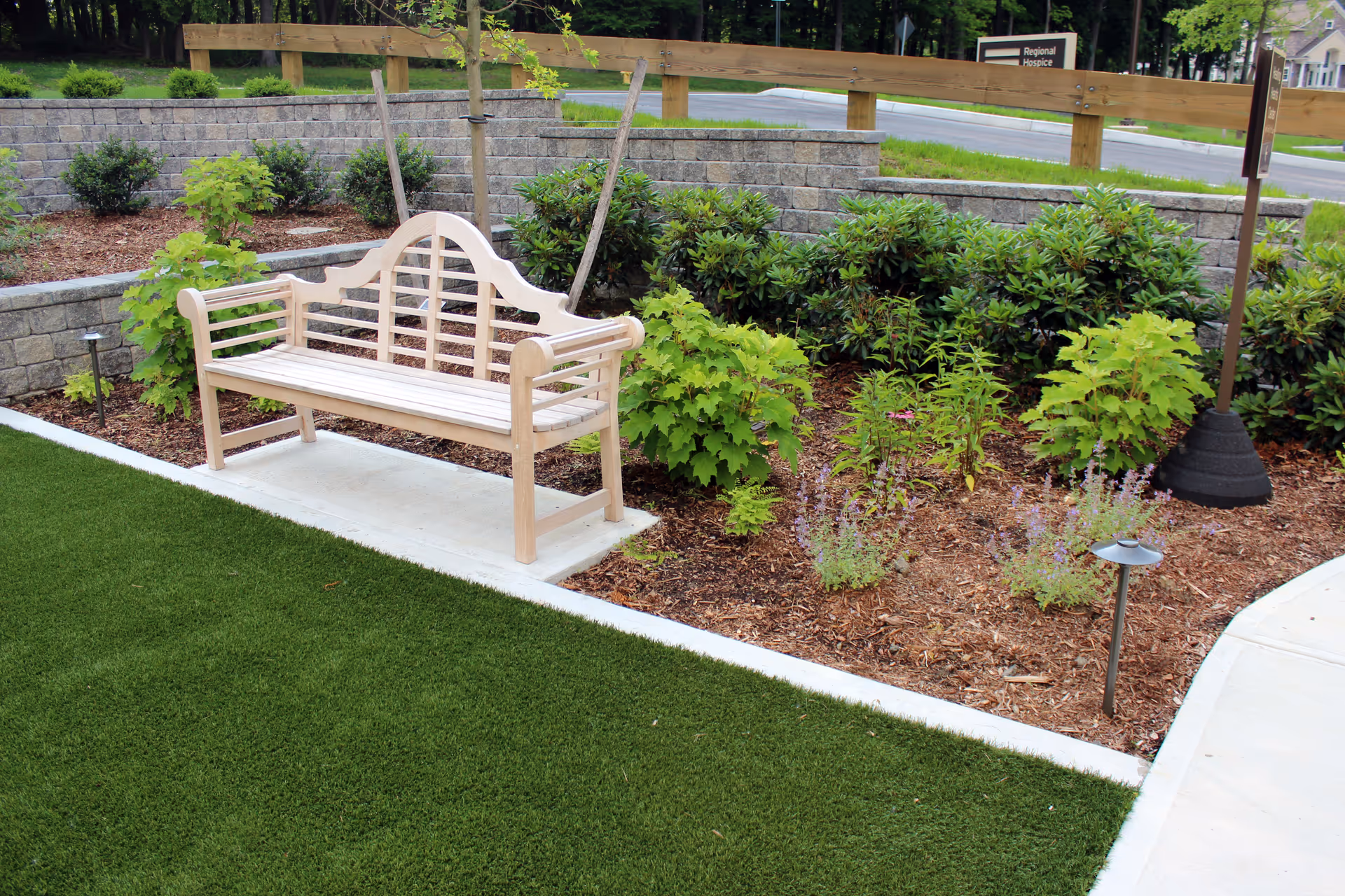 Wooden bench sits in a landscaped garden outside a hospice facility.