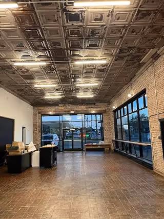 Empty lobby area with brick walls, tiled floor, large windows, and decorative ceiling tiles.
