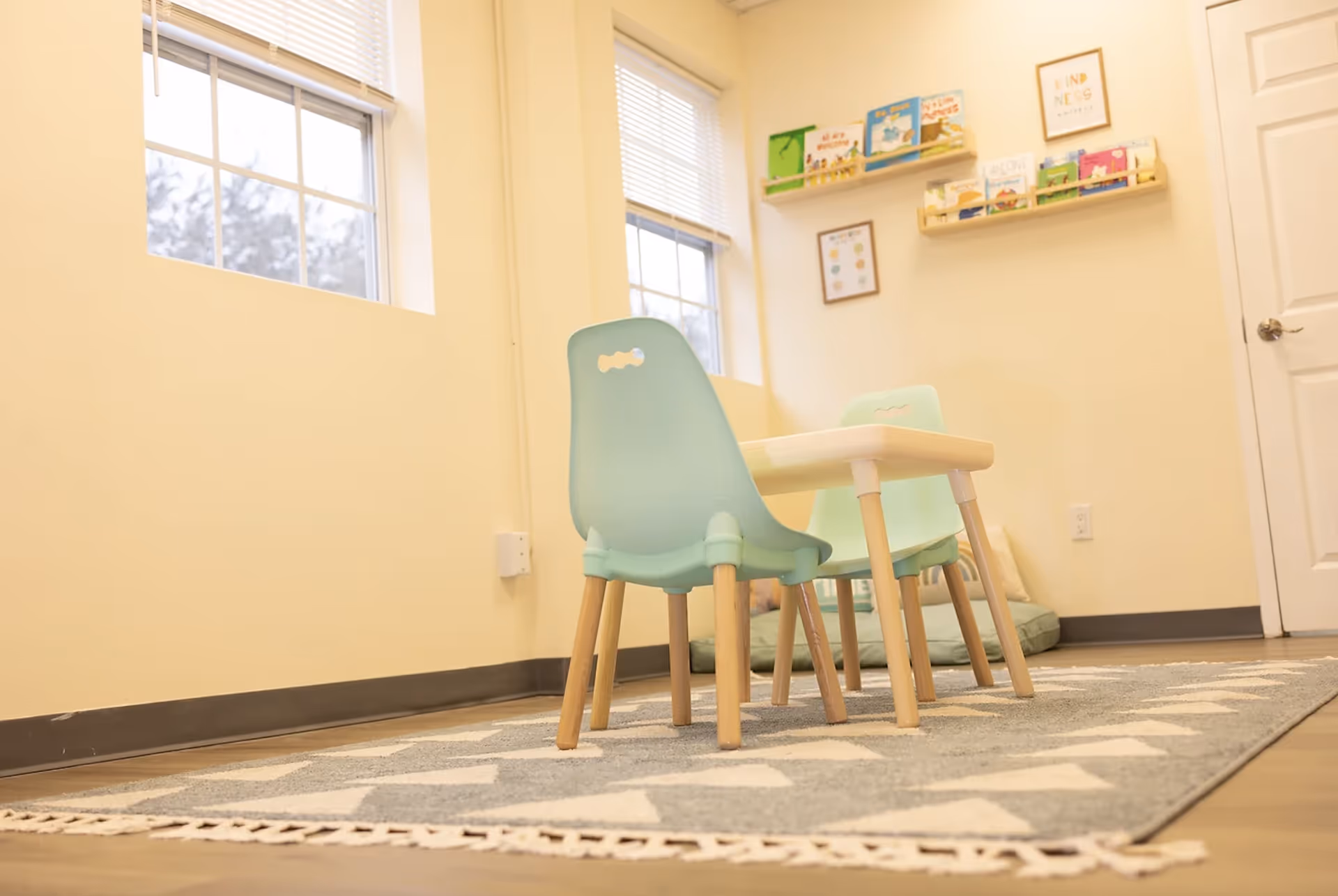 Bright, child-sized teal chairs surround a small table in a cozy activity corner.