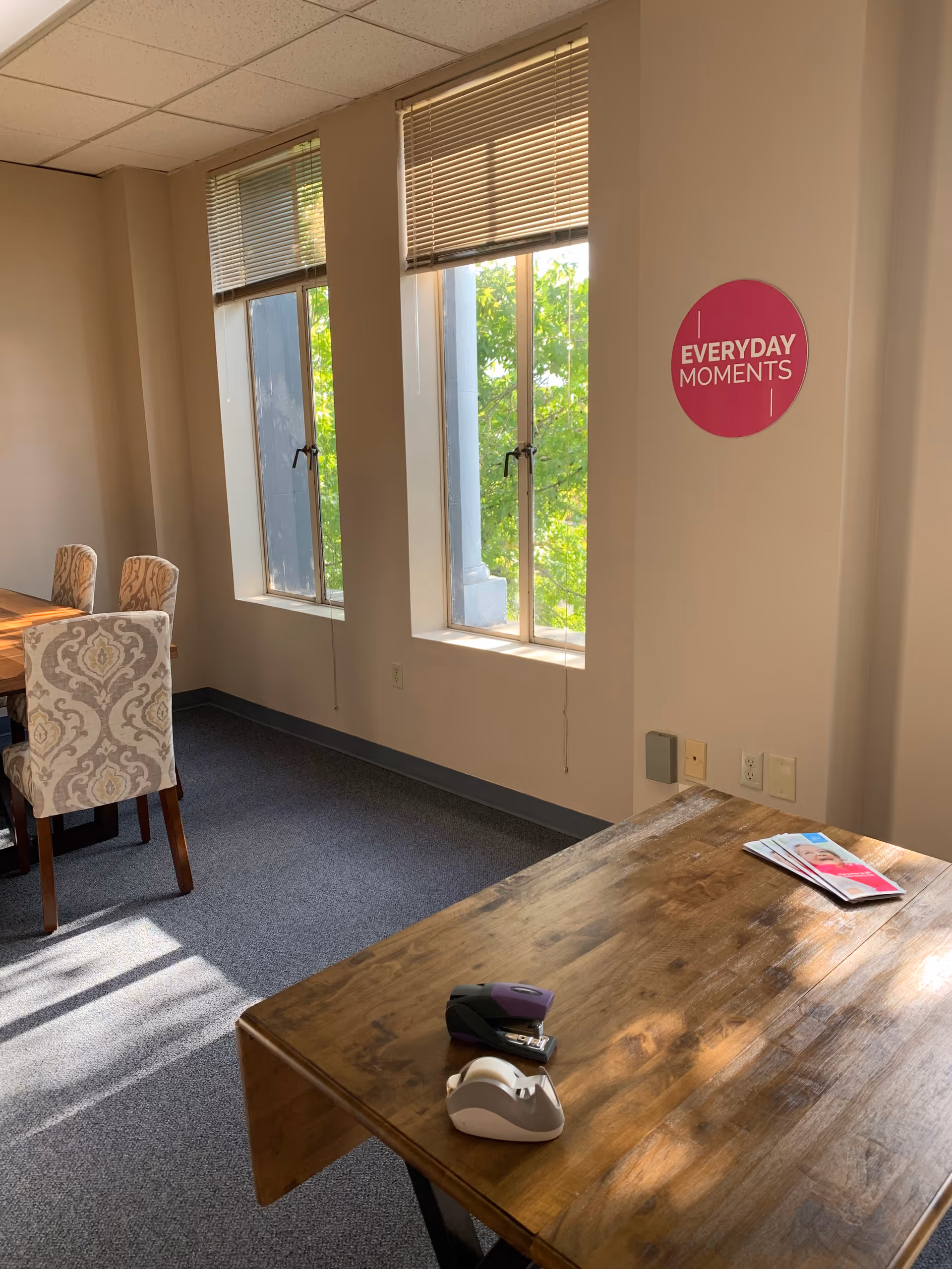 Interior dining area with a wooden table, patterned chairs, and a pink 'Everyday Moments' sign.