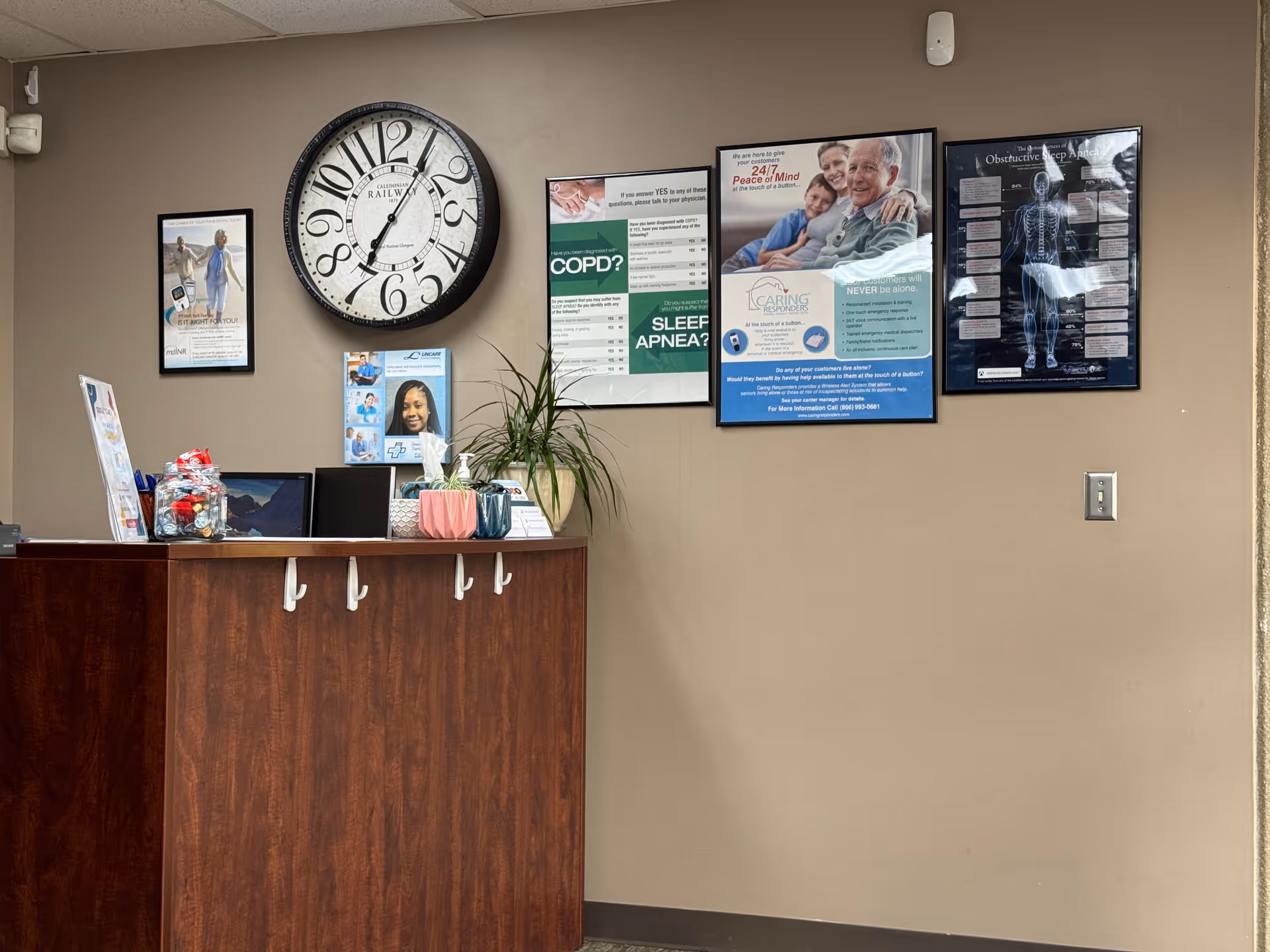 Reception area with a dark wooden counter, wall clock, plant, and posters on the wall.