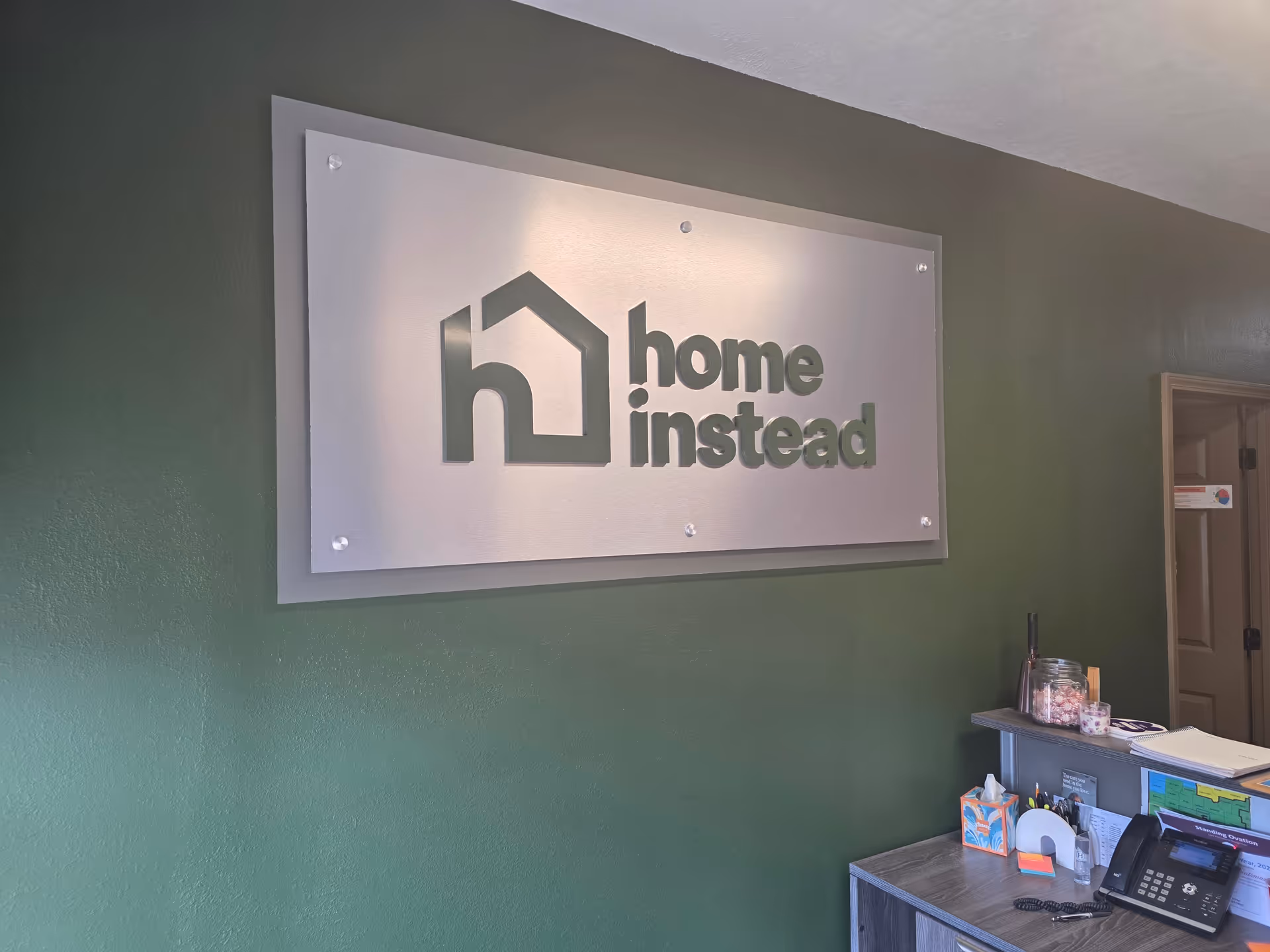 Indoor reception area with a large Home Instead sign on a green wall.
