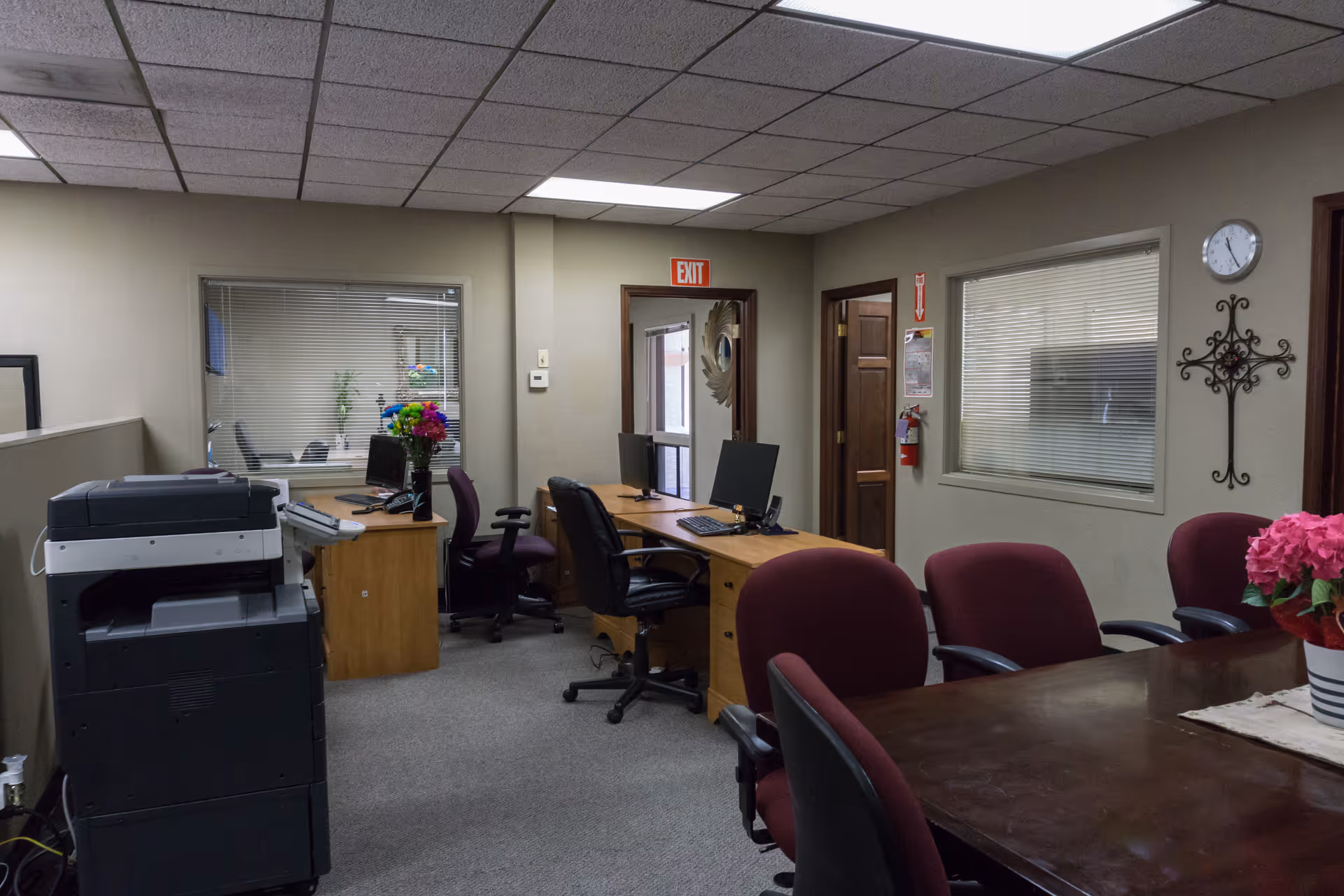 Office area with desks, computers, chairs, a conference table, and a printer in a living facility.