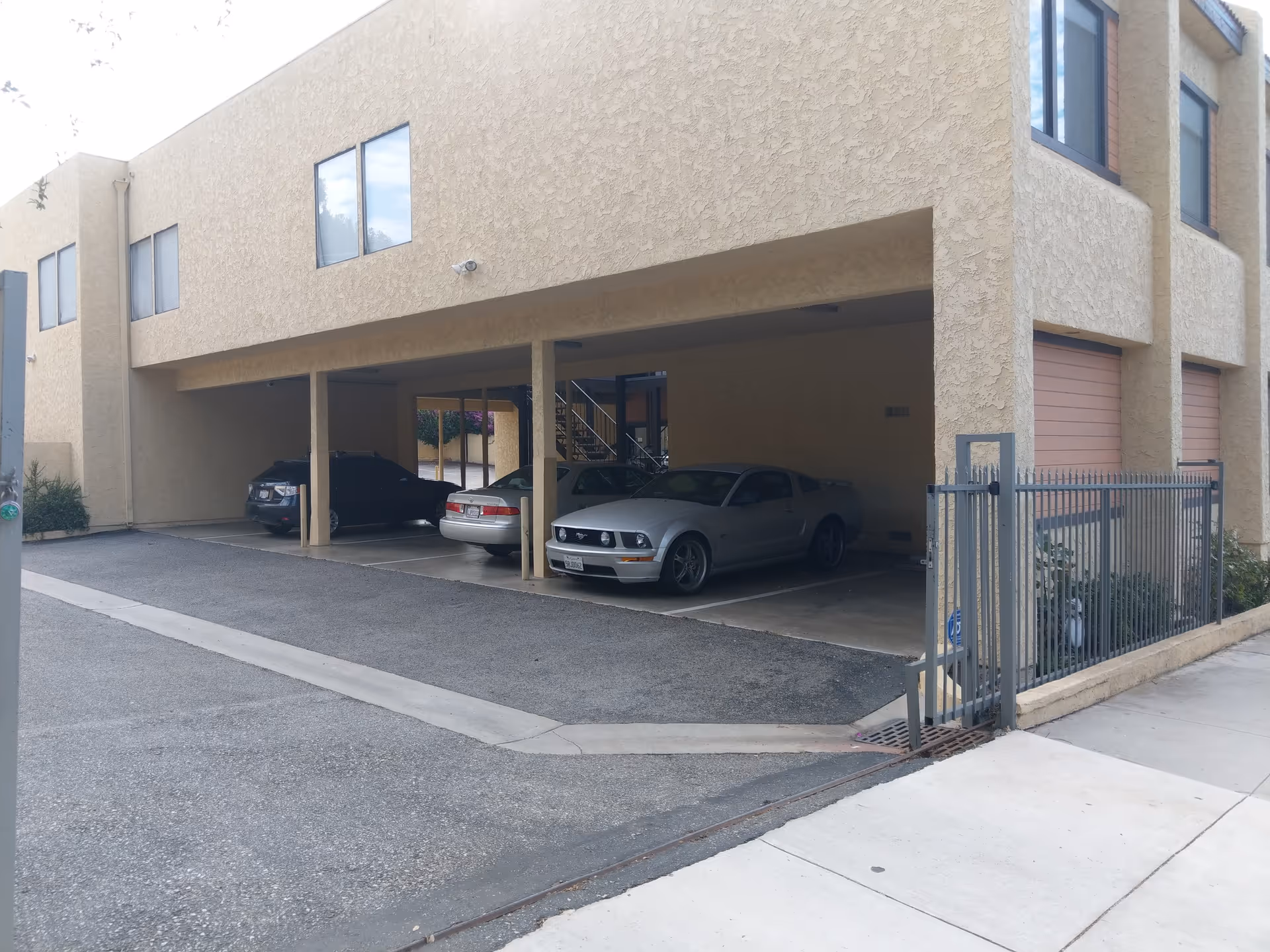 Beige multi-level building with a covered parking area and parked cars.