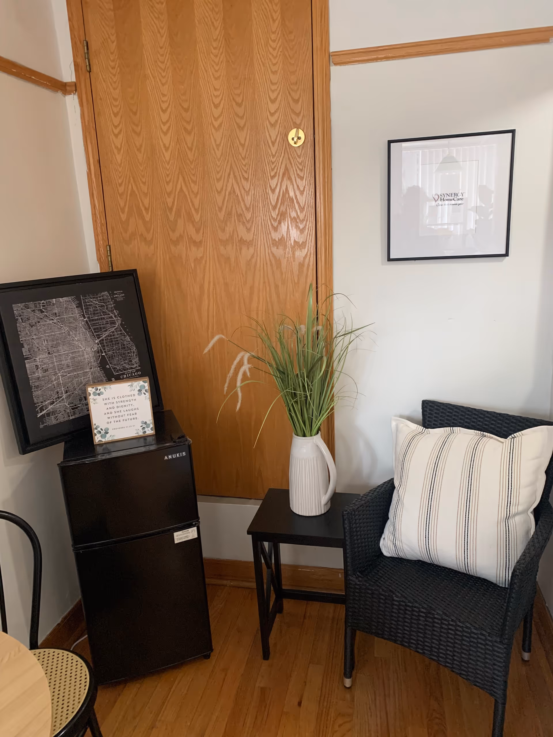 Cozy corner with wicker chair, plant, mini-fridge, framed art in a senior living interior.