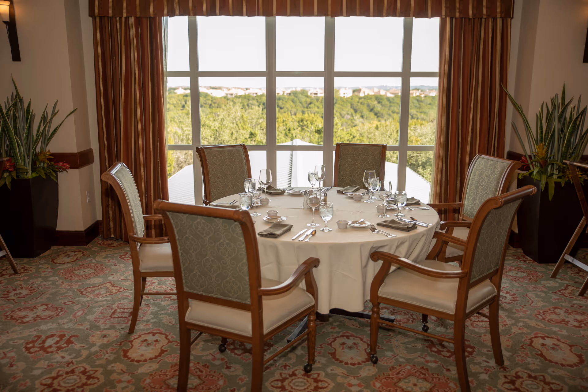 Round dining table set for six in an elegant, sunlit dining room.