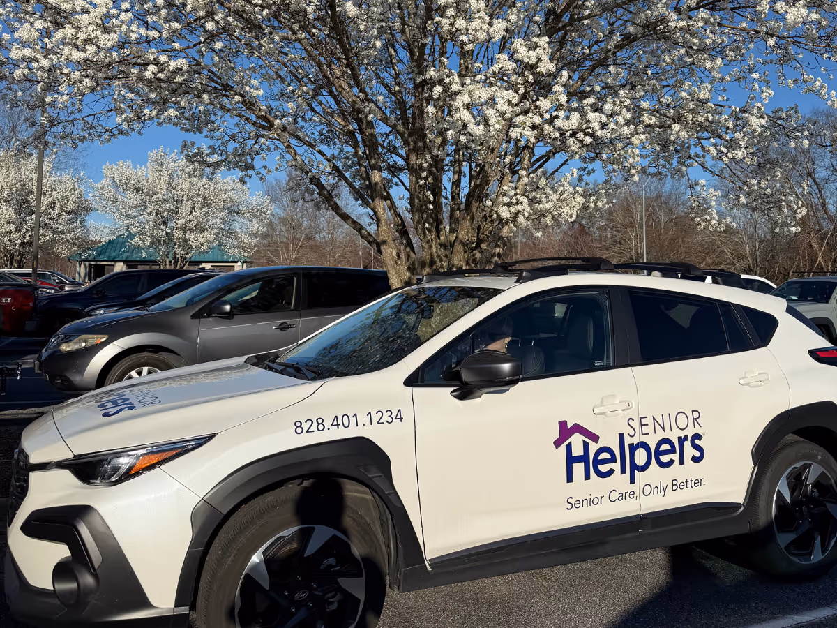 White Senior Helpers vehicle in a parking lot with blooming trees and blue sky.