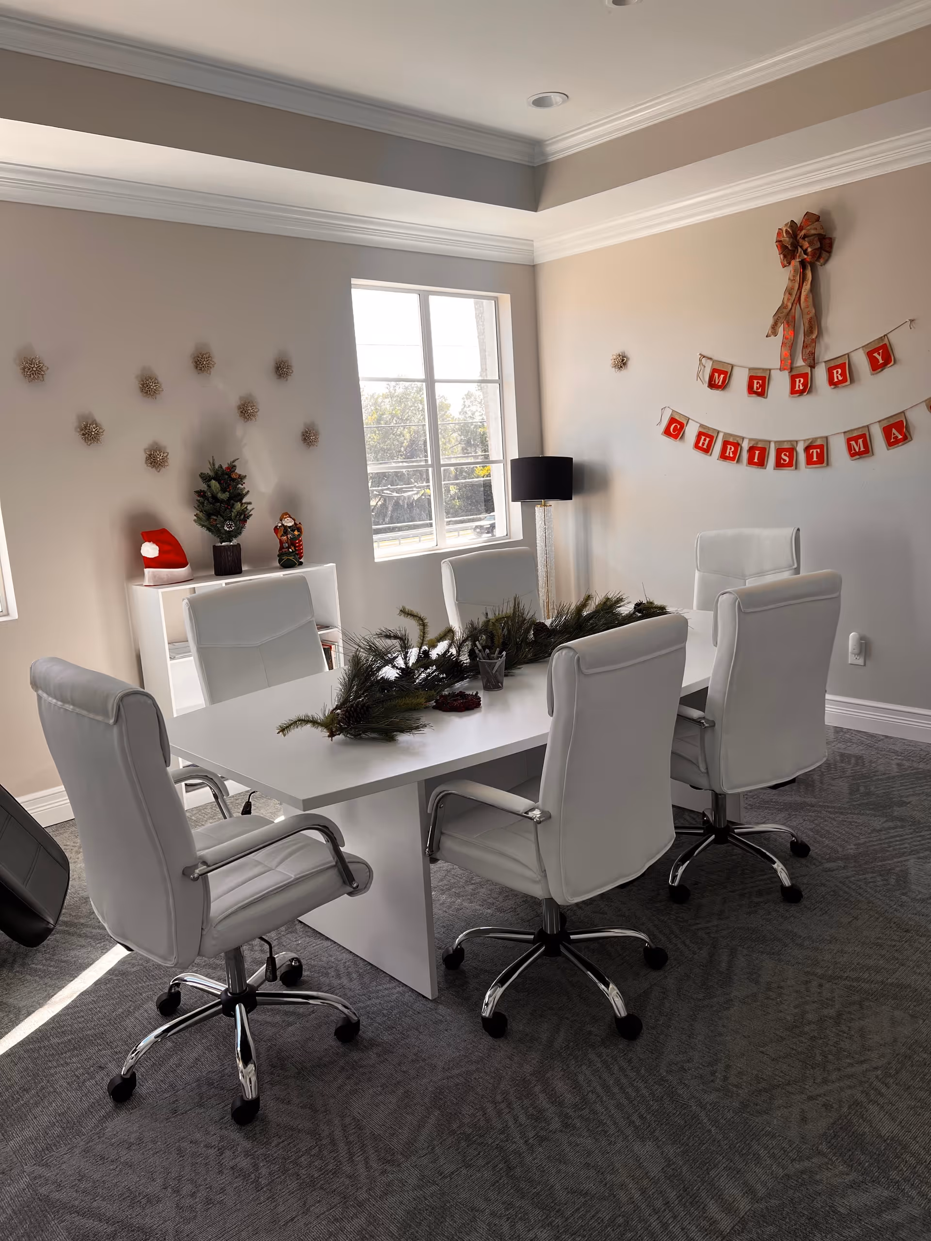 A bright white dining table with several white chairs and holiday decorations in a meeting room.