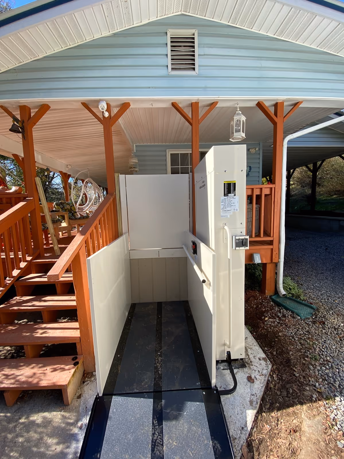 Blue house exterior with wooden porch, stairs, and a vertical wheelchair lift ramp
