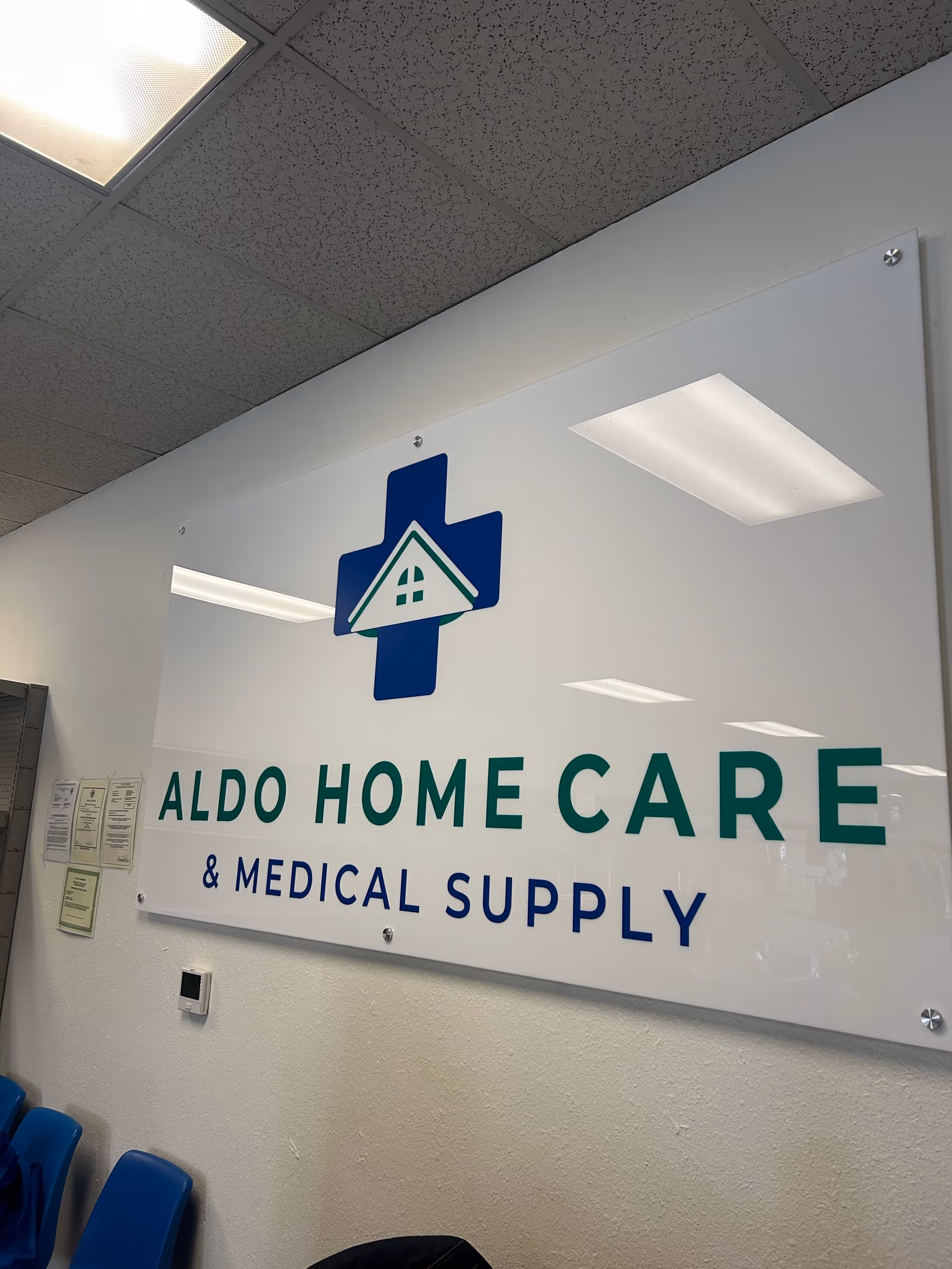Interior wall sign reading Aldo Home Care and Medical Supply with blue chairs nearby.