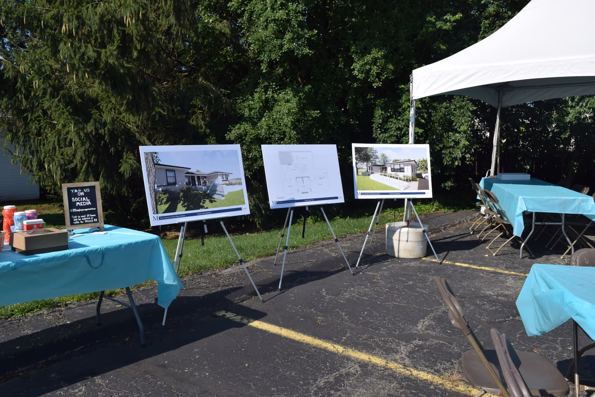 Outdoor display setup with architectural renderings on easels under a white canopy.