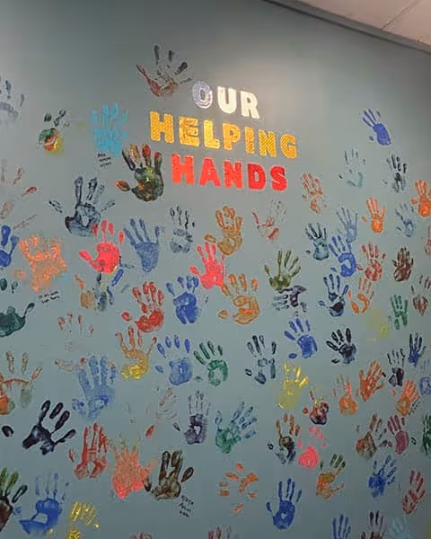 A wall covered in colorful handprints with the words 'Our Helping Hands'.