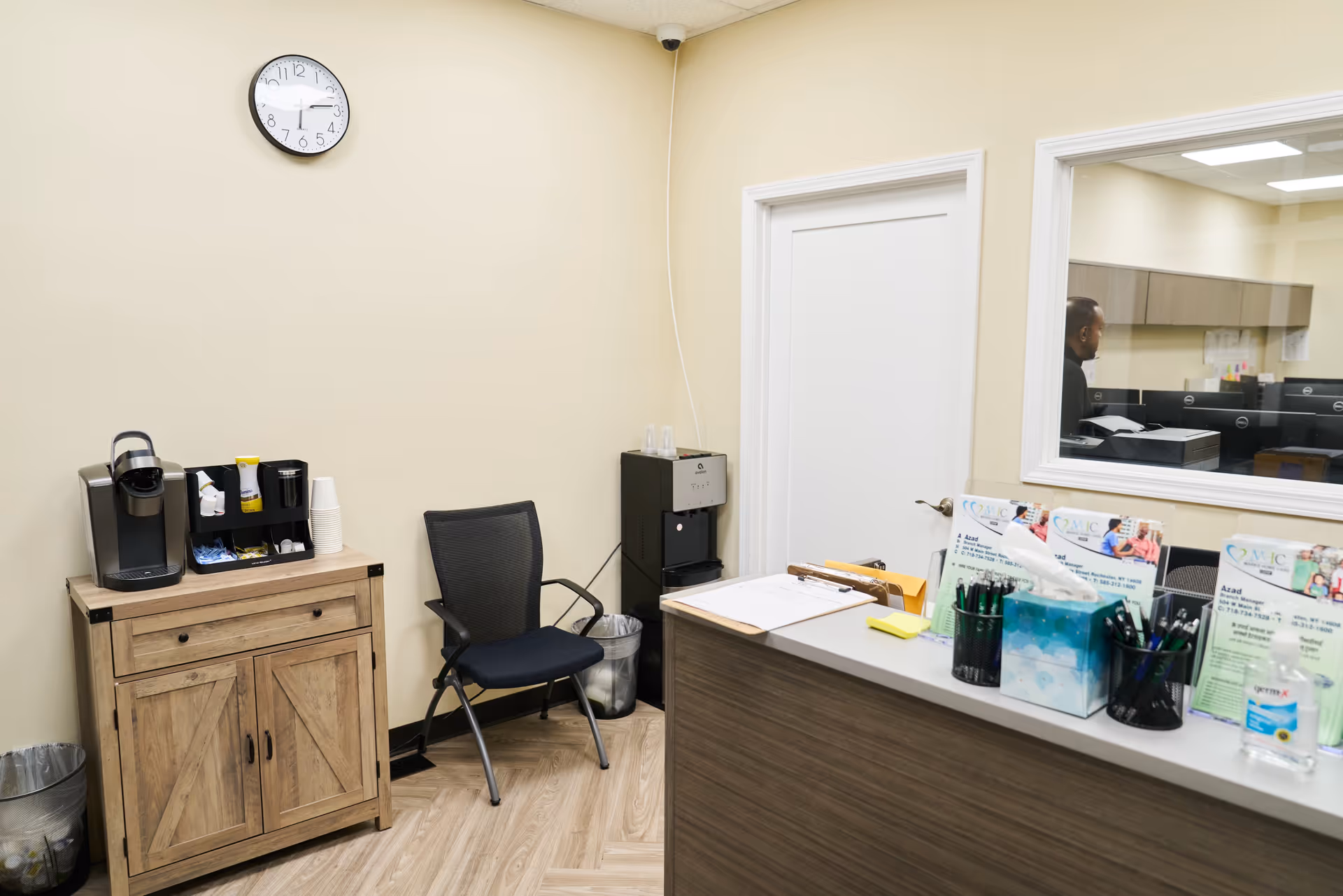 Reception area with coffee station, chair, desk, and a view into a staff workspace.