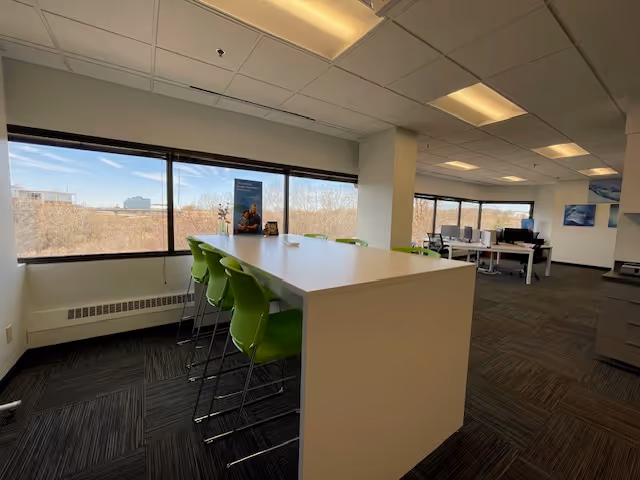Bright interior common area with a white high table, green chairs, and large windows.