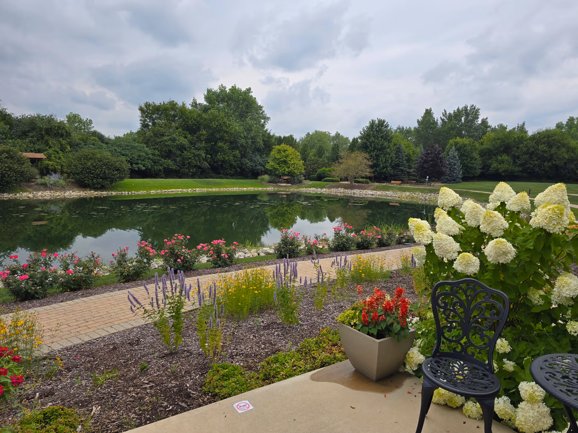 A landscaped garden with a pond, colorful flowers, and metal patio chairs.