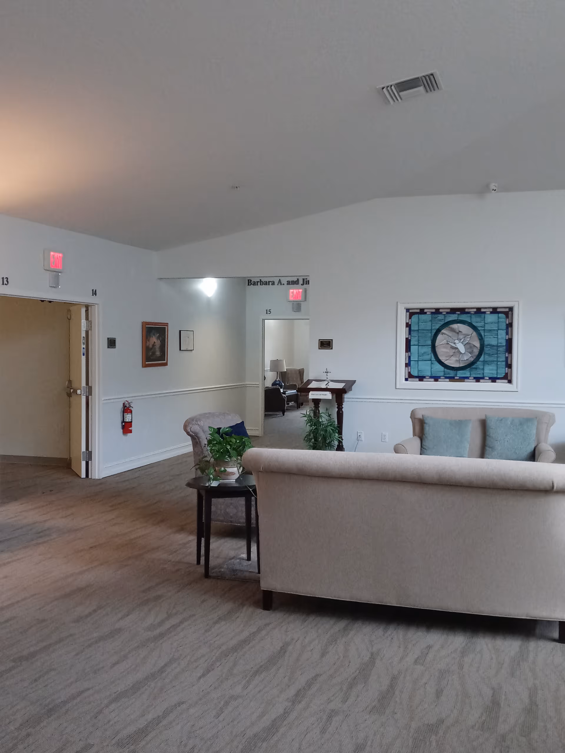 Spacious lounge area with beige sofas, a side table, plants, and wall art.