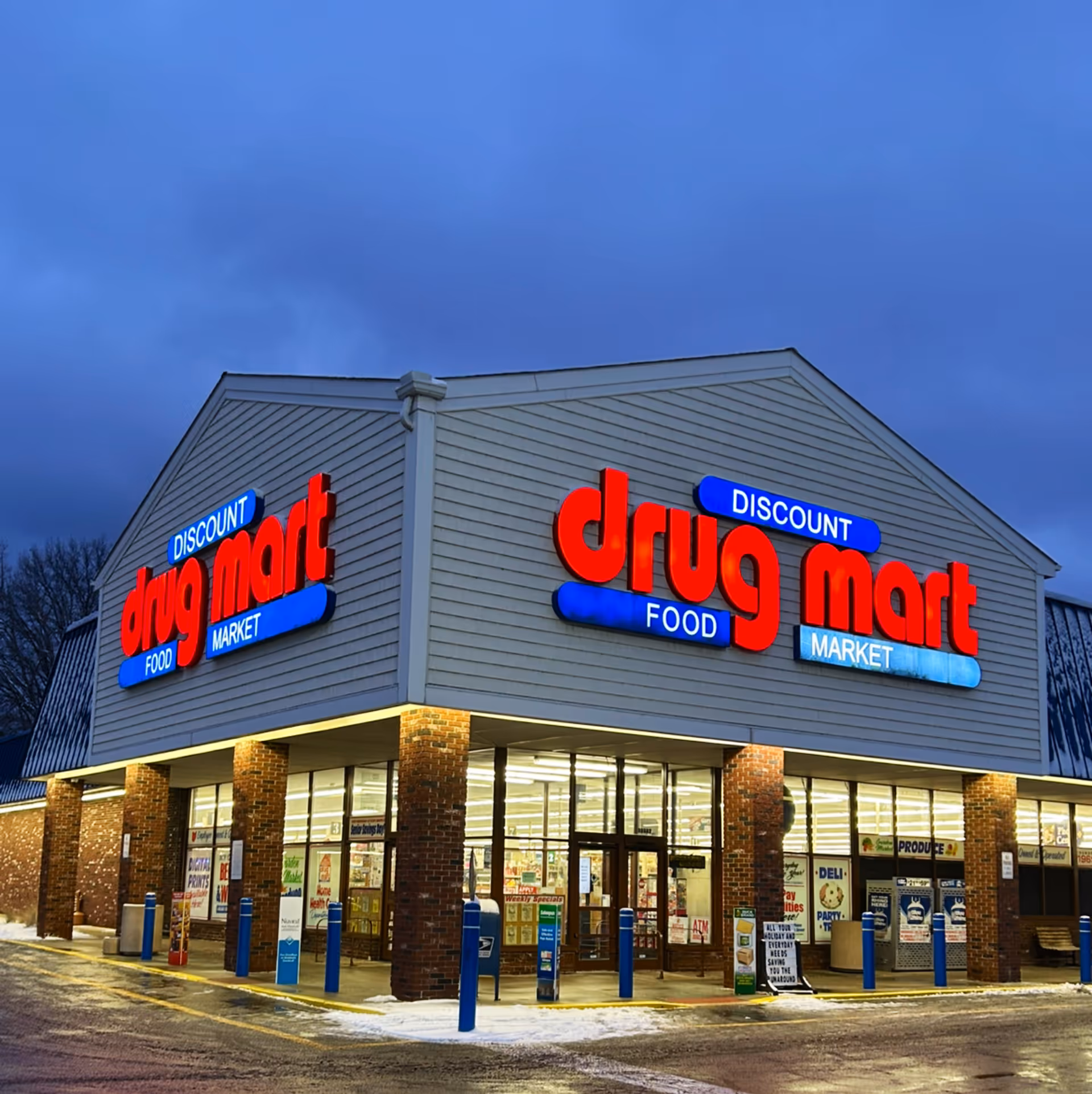 Exterior view of Discount Drug Mart storefront with red illuminated sign at dusk.