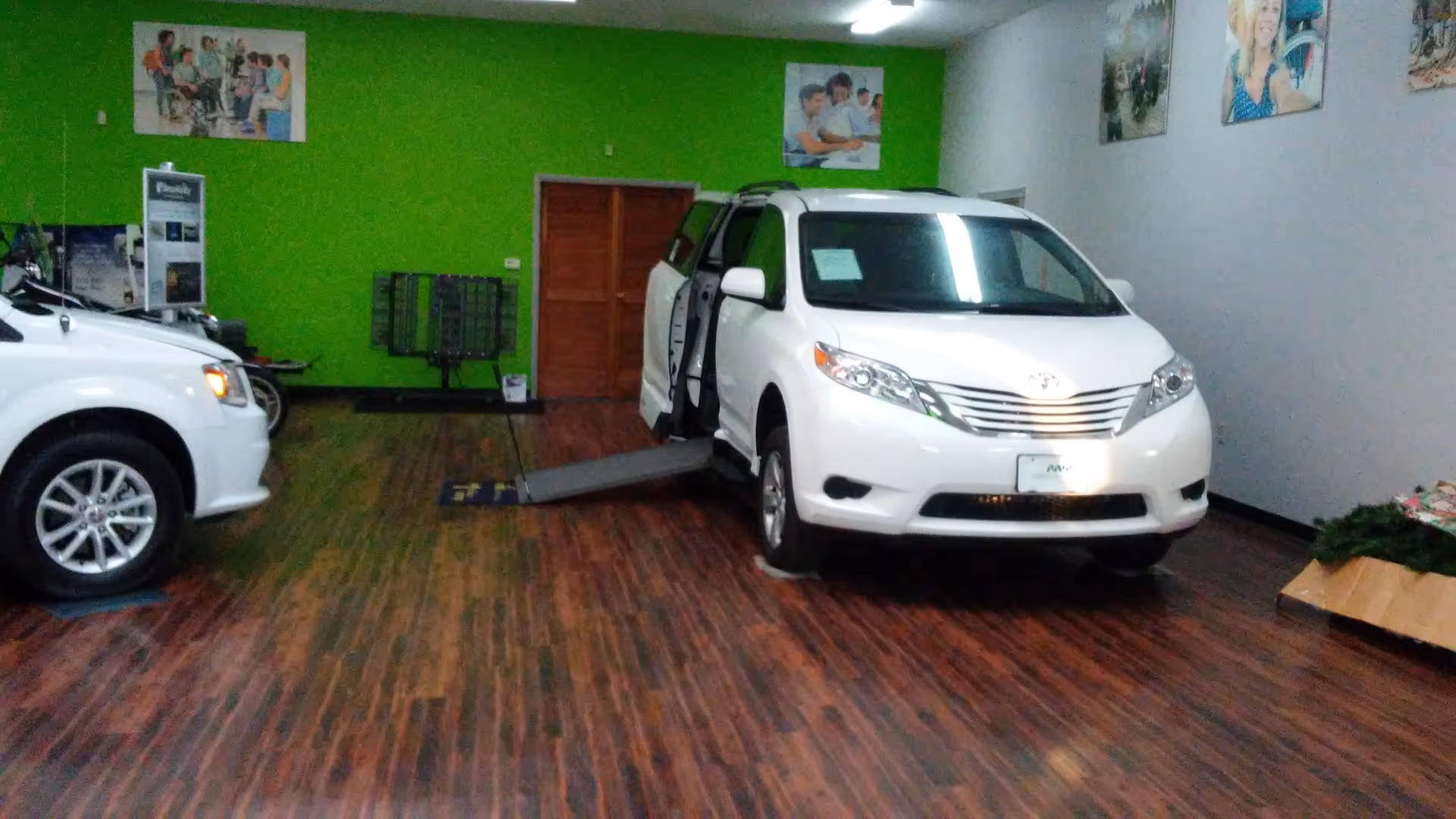 White mobility vehicles on display inside a showroom with a green accent wall and wood flooring.