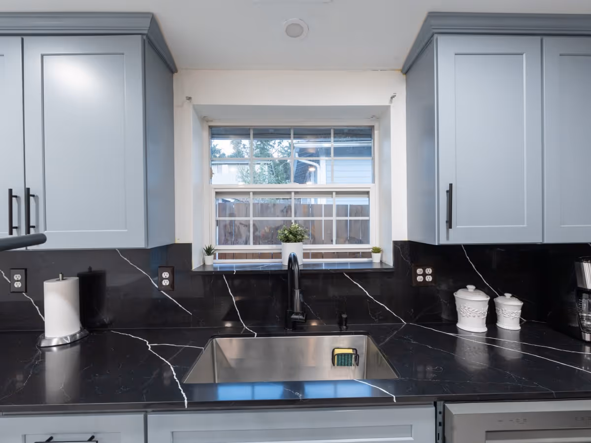 Blue cabinetry and black marble countertops frame a kitchen with sink under a window.