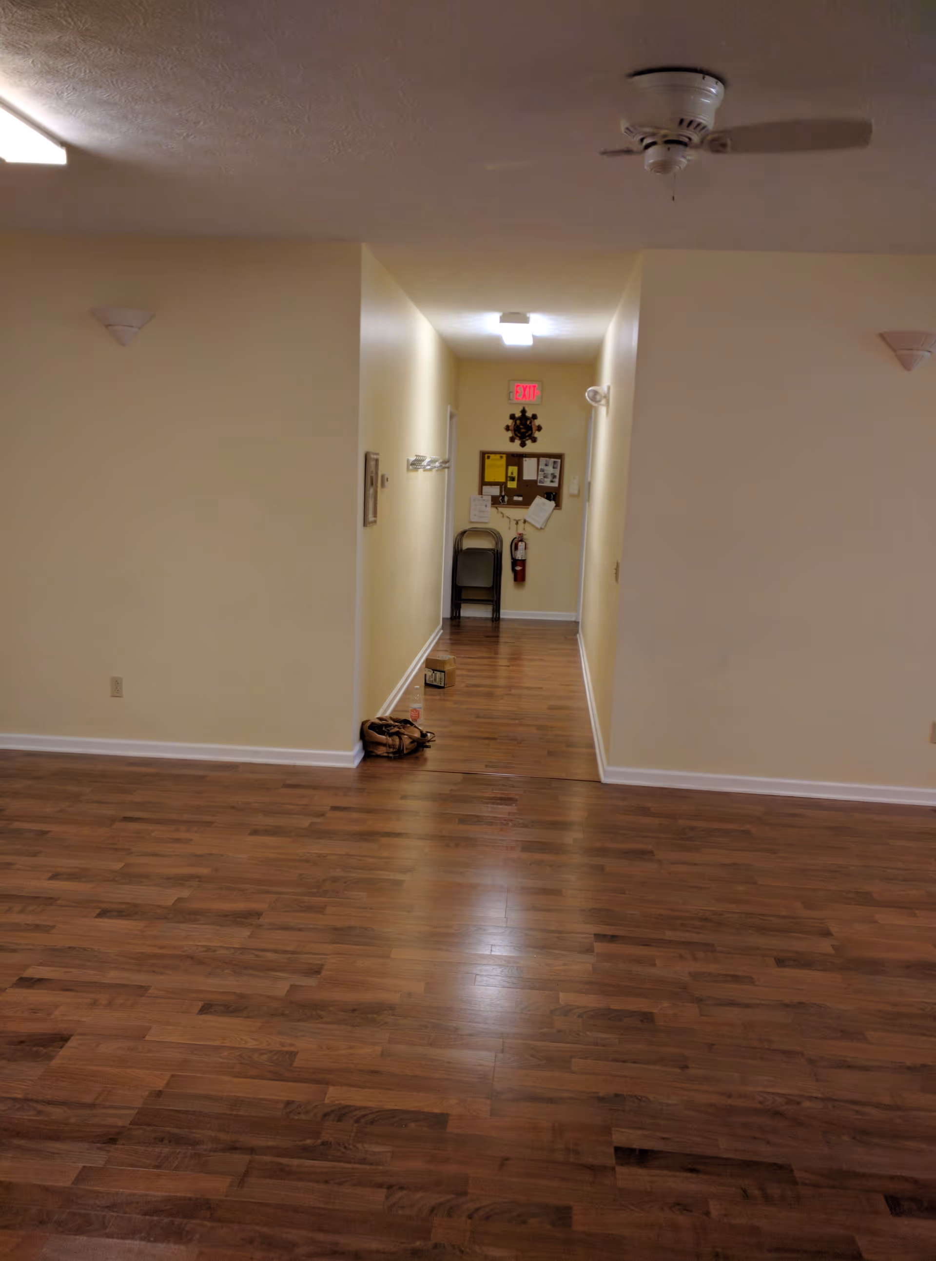 Long hallway in a senior facility with beige walls, wood floors, and a ceiling fan.