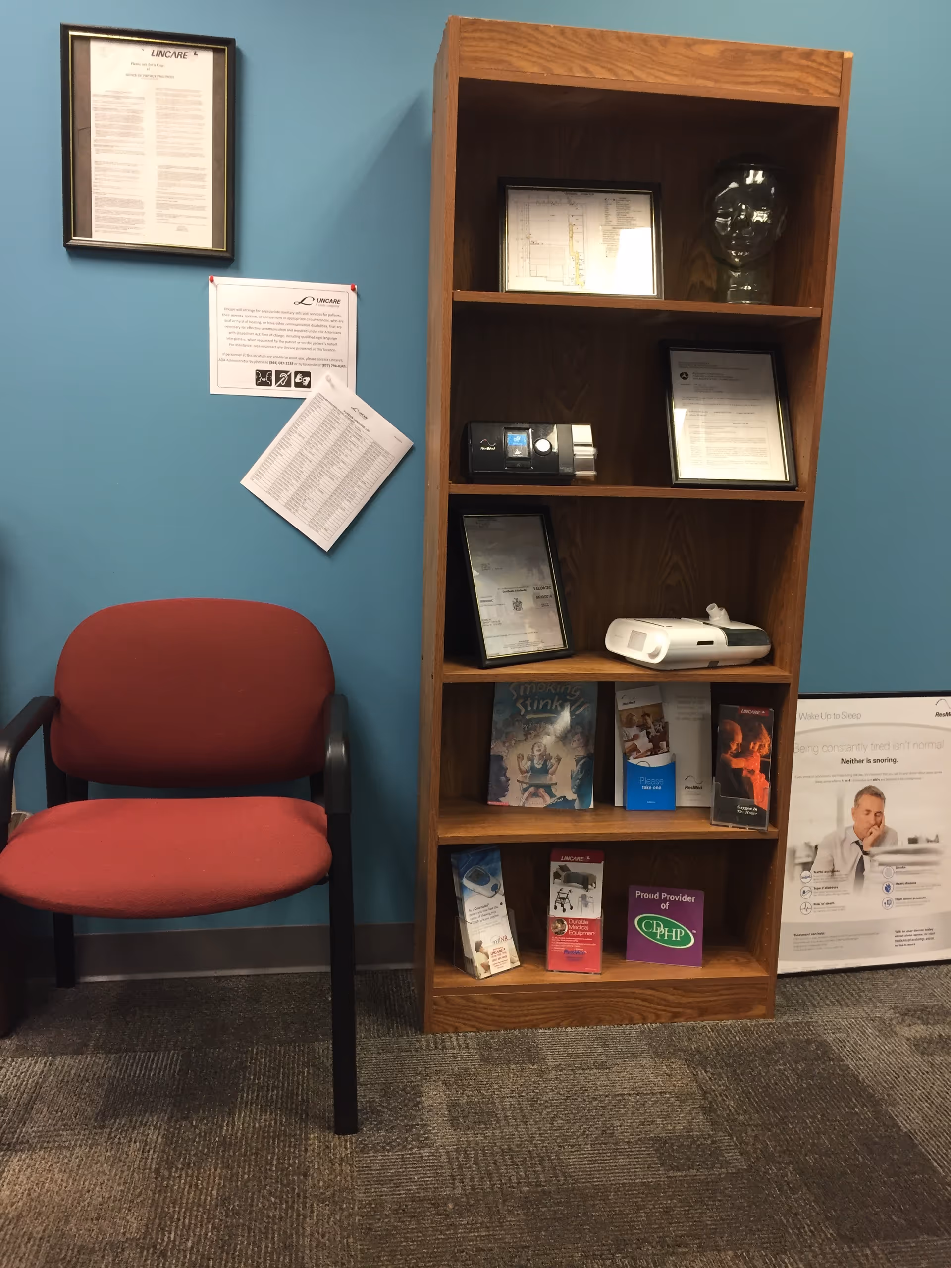 Red cushioned chair beside a tall wooden shelf filled with brochures against a blue wall