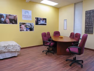 yellow-walled interior room with a wooden conference table, purple chairs, and a bed in the corner.