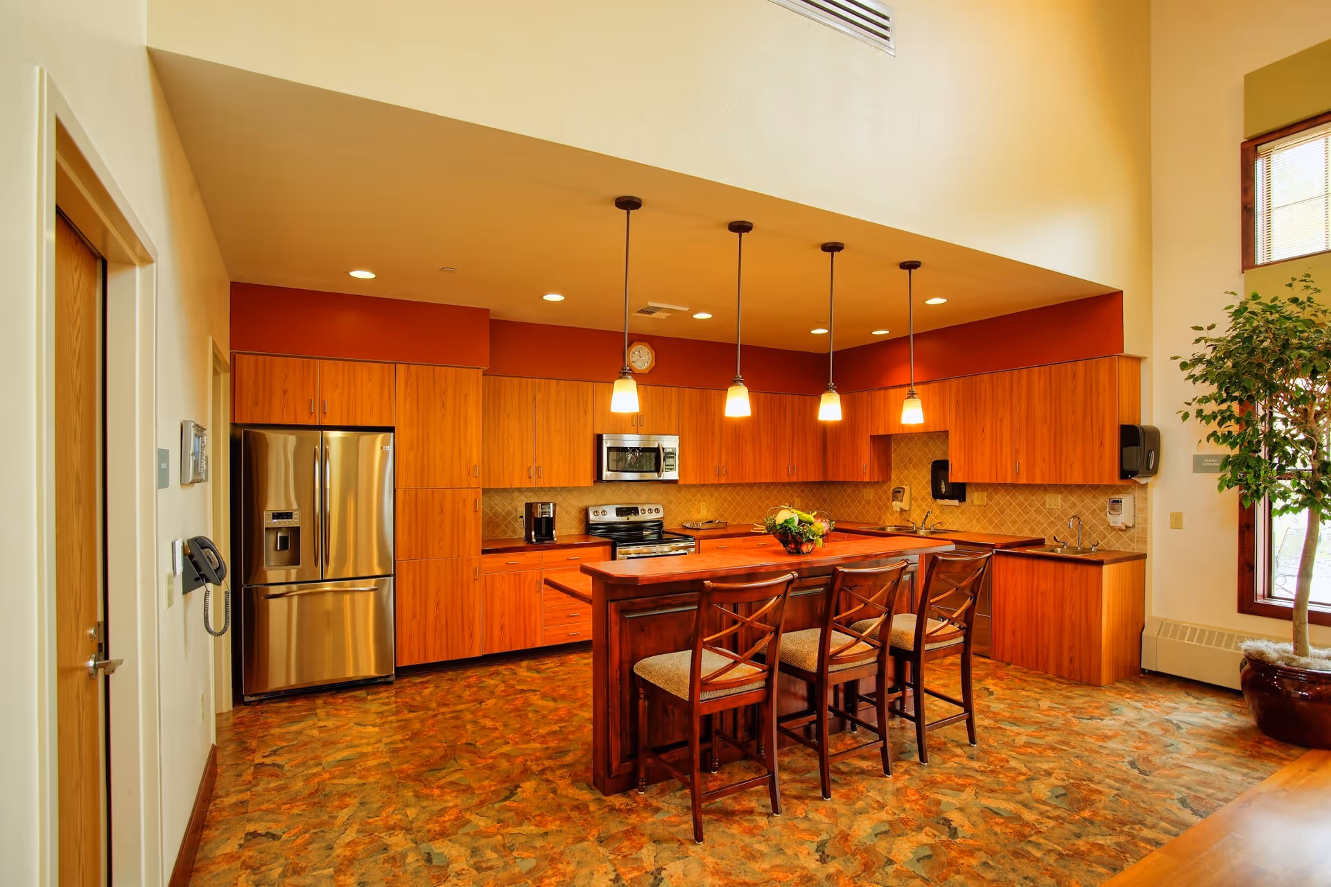 Modern communal kitchen with island, pendant lights, stainless steel appliances, and wooden cabinets.