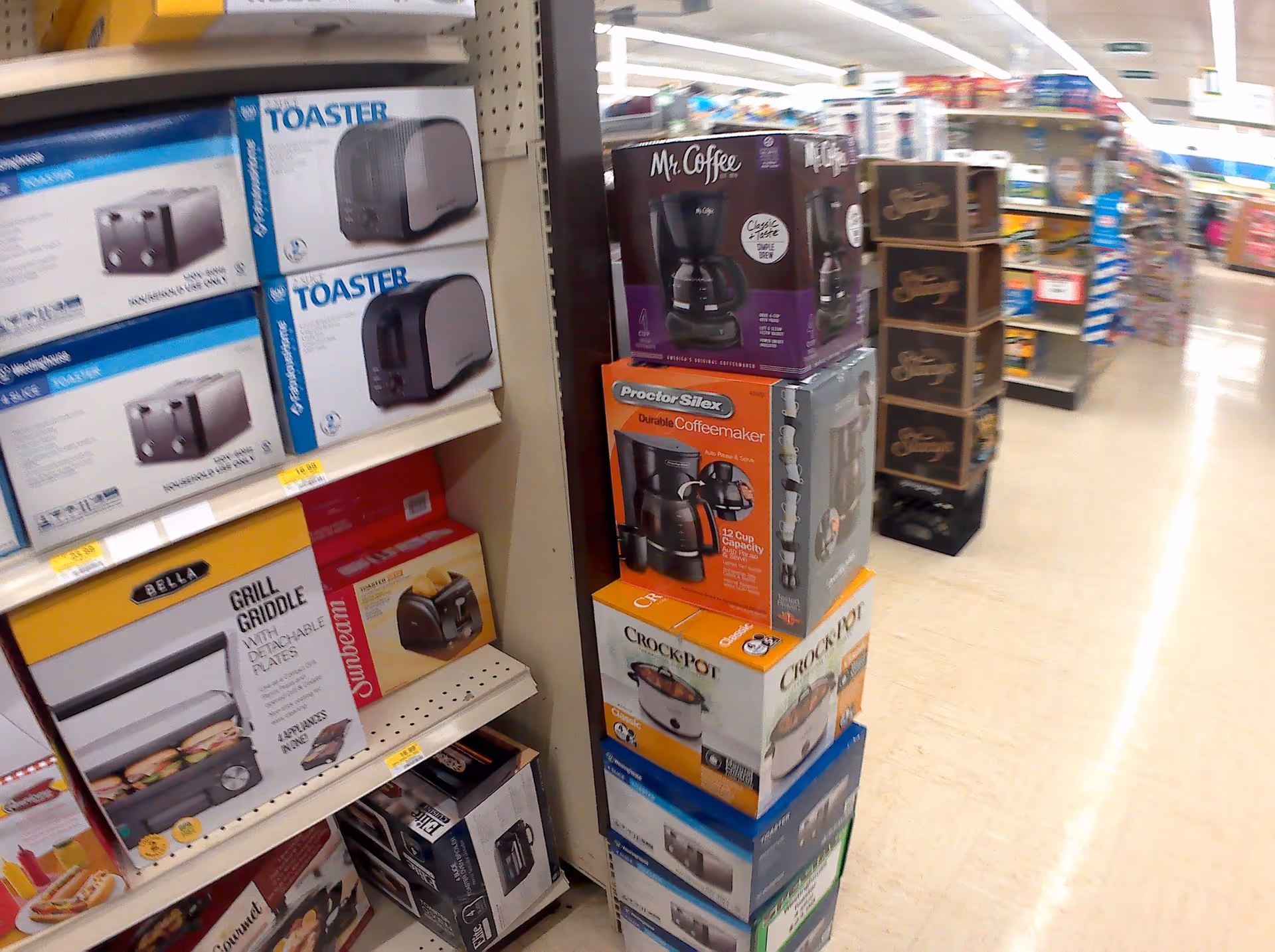Aisle of boxed small appliances (toasters, coffee makers) on store shelves.