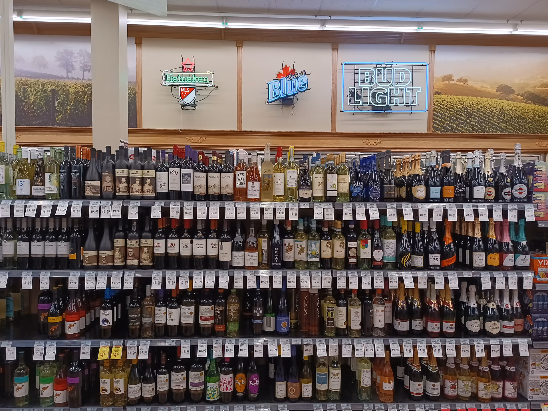 Long grocery-style aisle filled with bottled wines and neon beer signs on the wall.