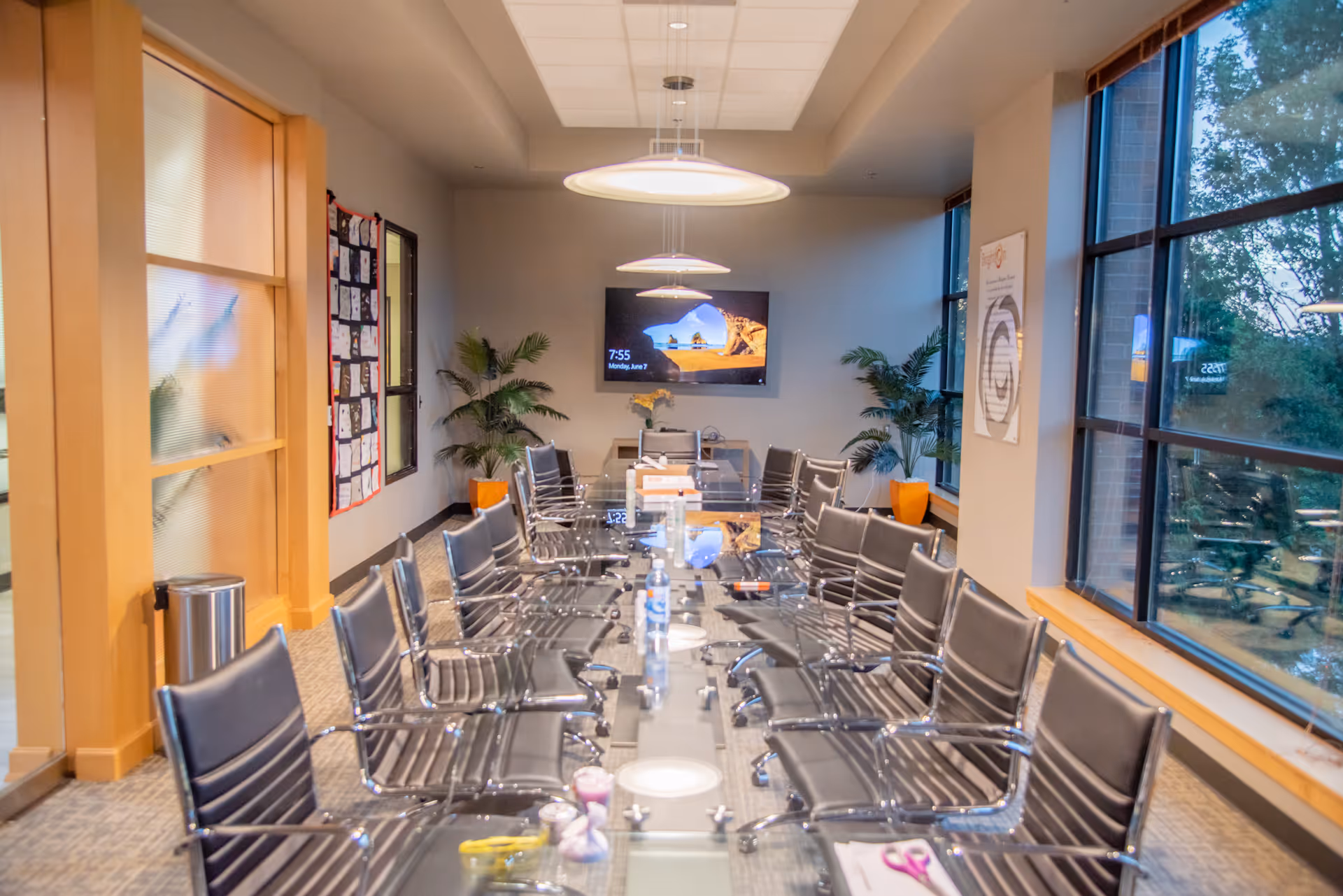 Conference room with a long glass table, black chairs, and a wall-mounted TV.