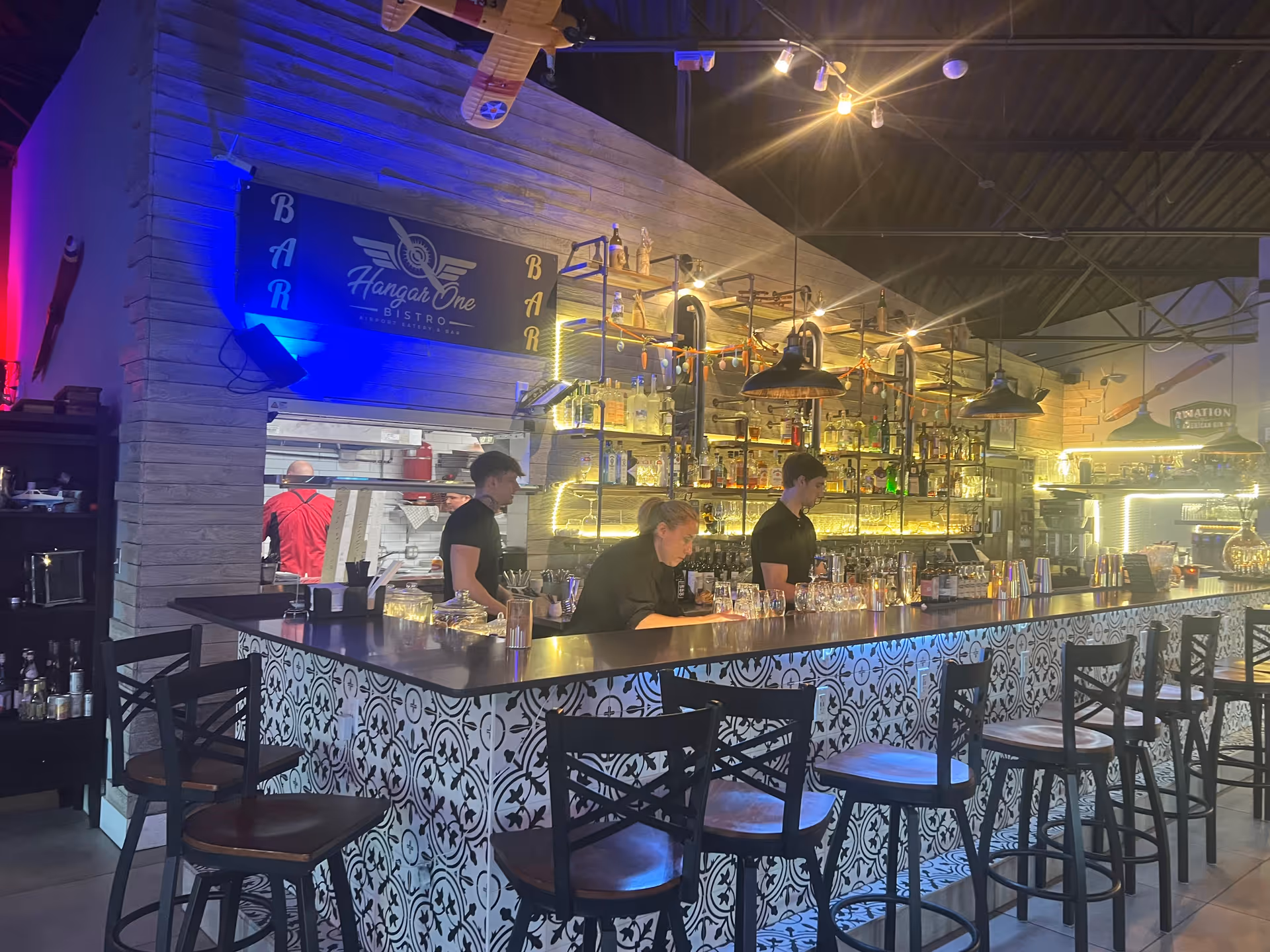 A stylish bar interior with a long counter, stools, and illuminated shelves.