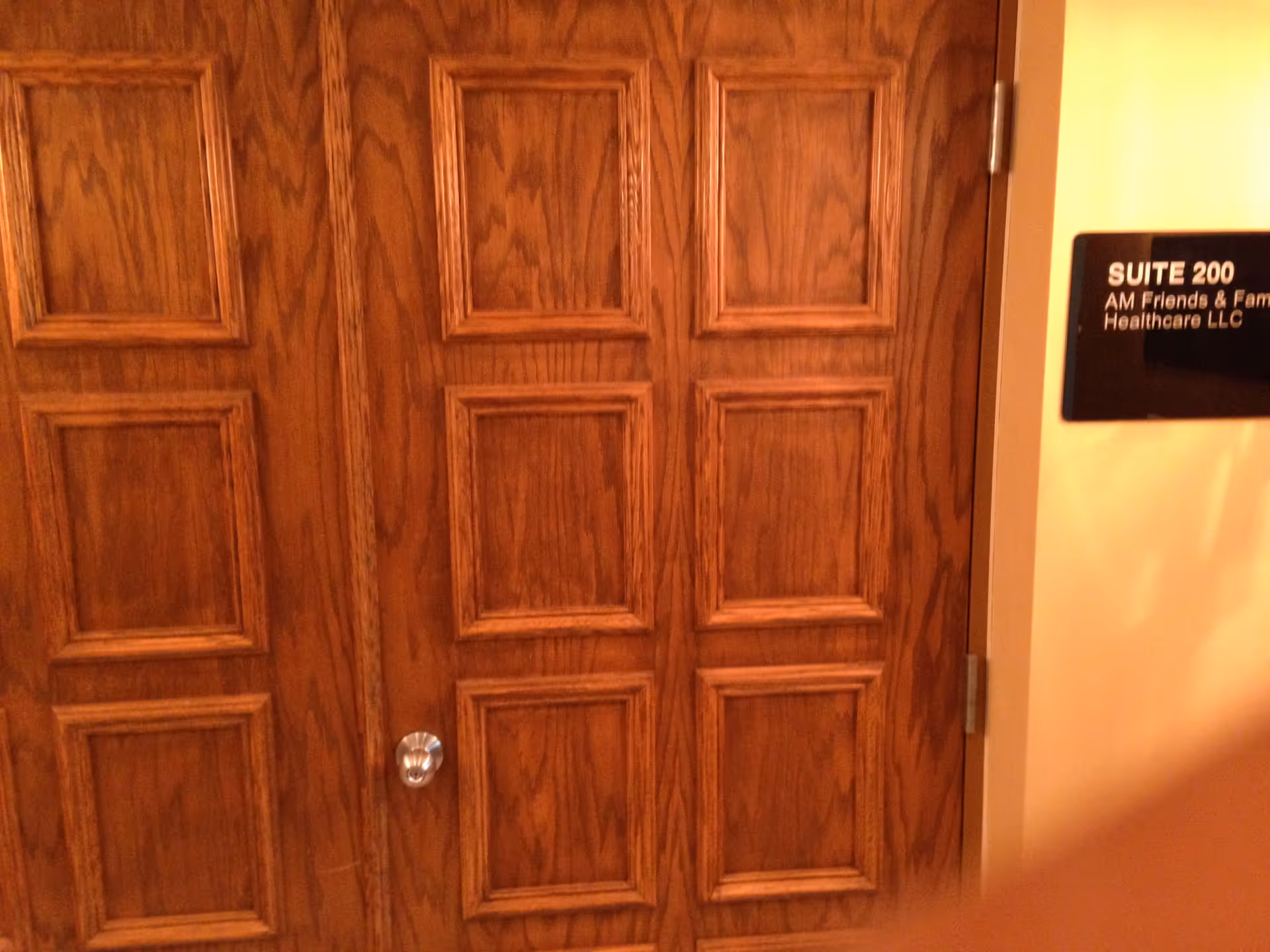 Wood paneled interior doors with a Suite 200 sign mounted on the wall.
