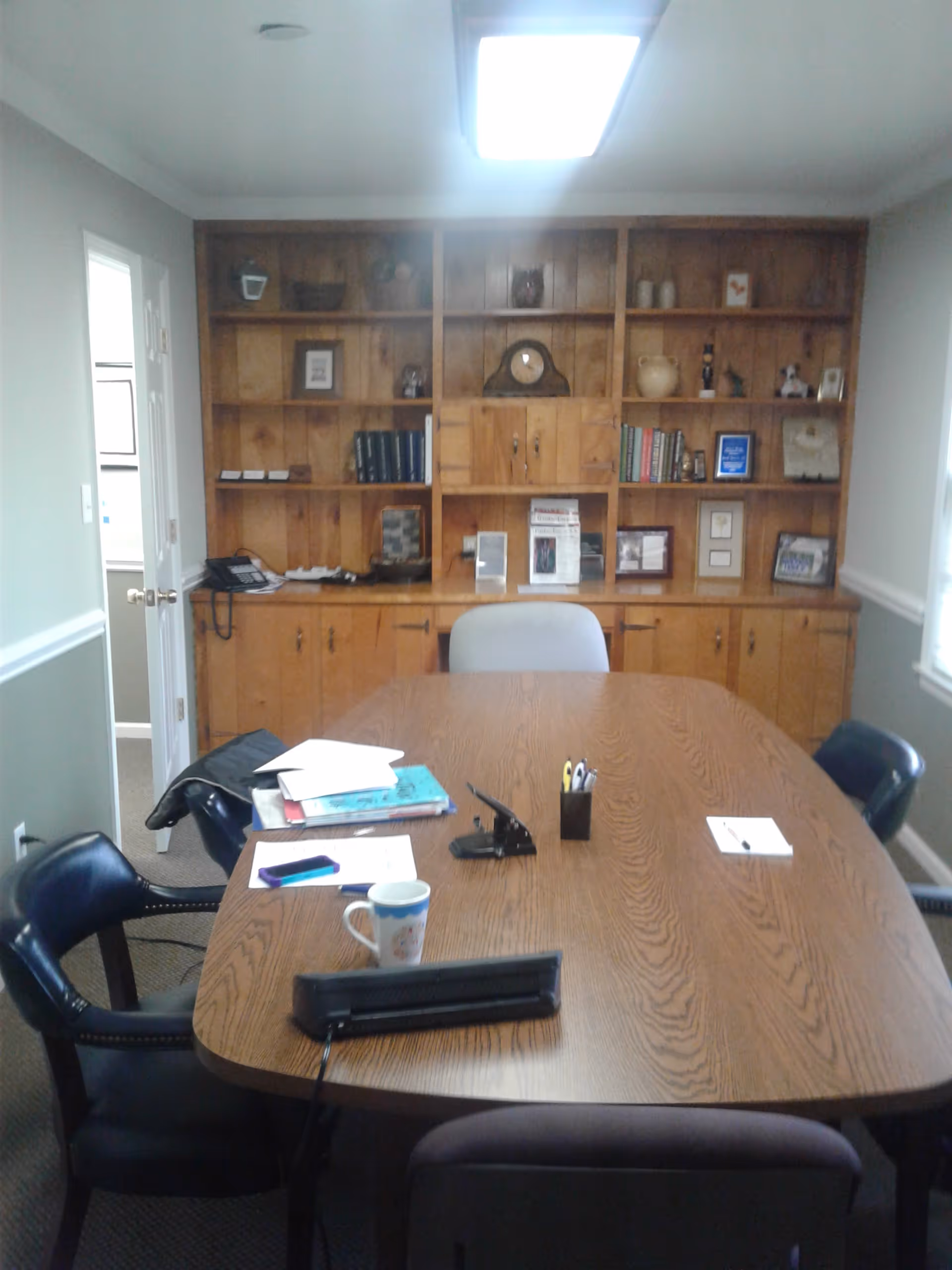 Wood conference table with chairs in a furnished office; bookshelf wall behind.