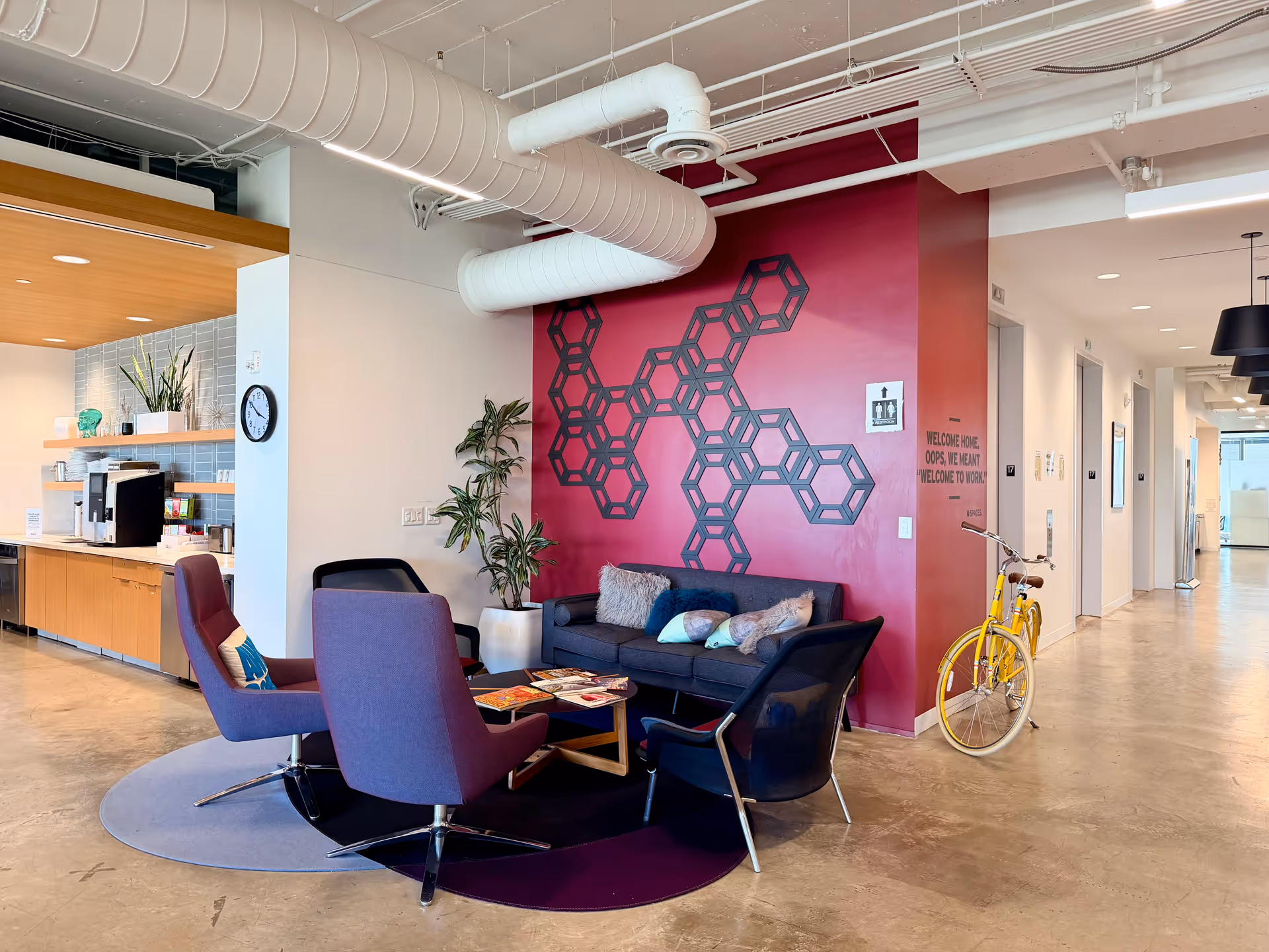 Contemporary lounge area with magenta wall, hexagon art, and a yellow bicycle.