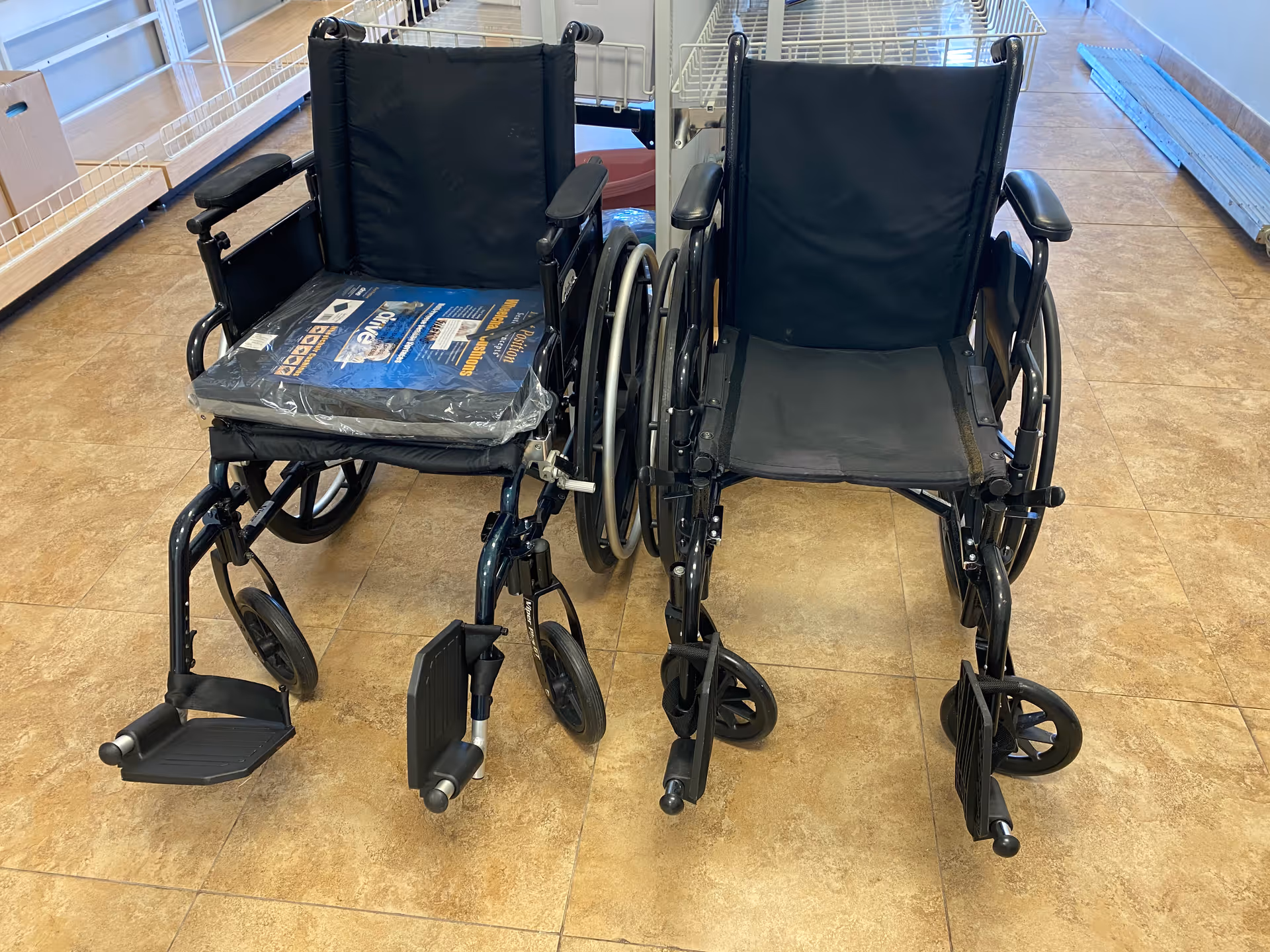Two black wheelchairs are parked in a tiled facility hallway.