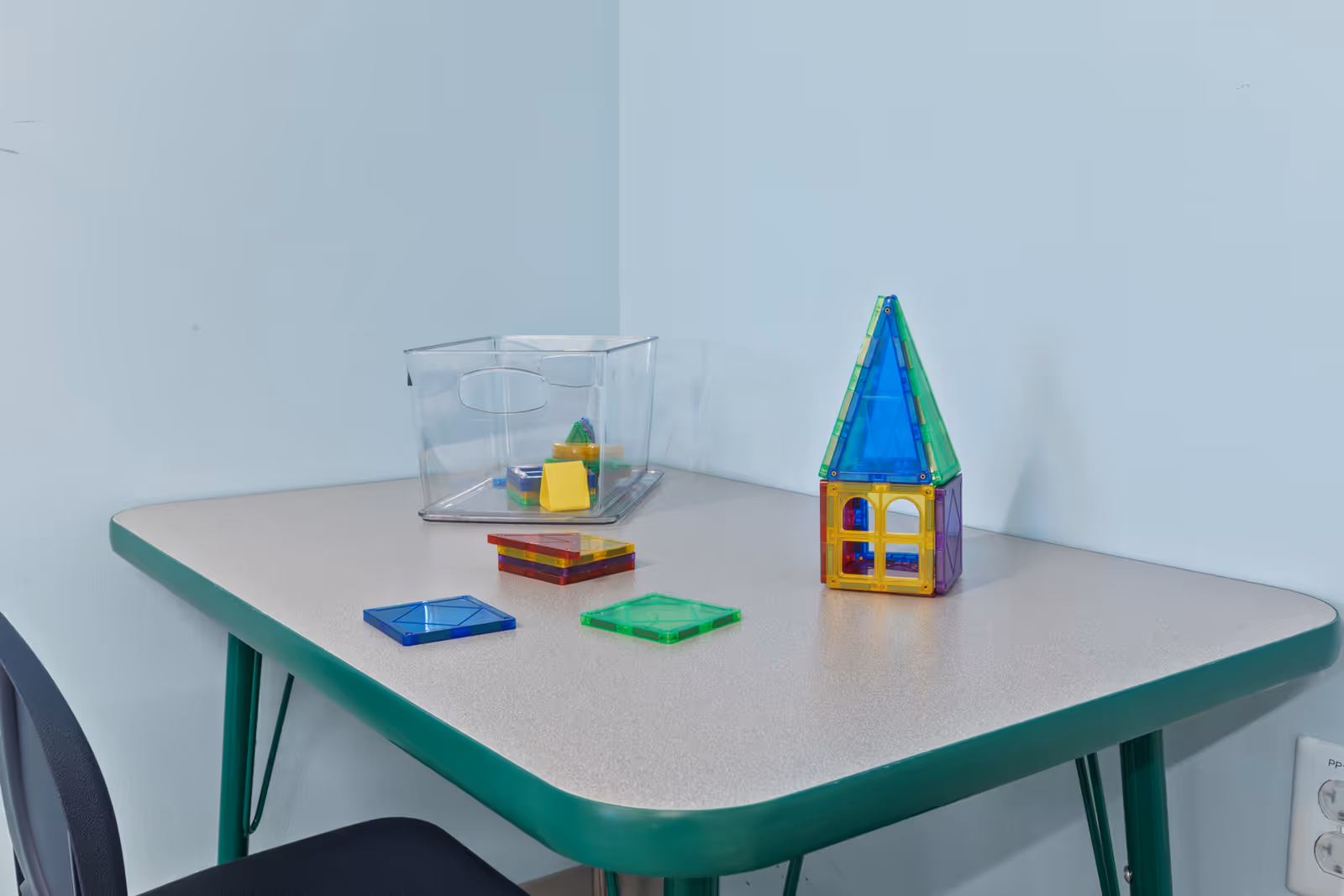 Colorful magnetic tiles sit on a rounded table in a pale-blue room.