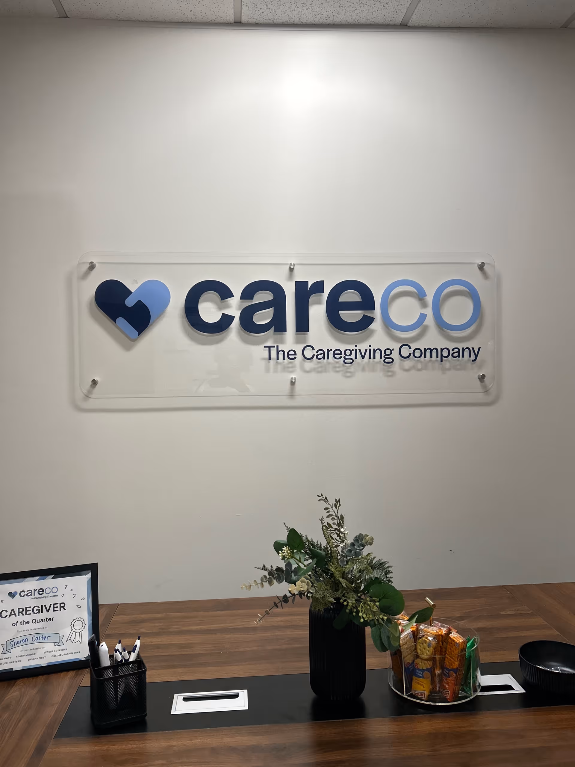 CareCo sign mounted on wall above a reception desk with a plant and snacks.