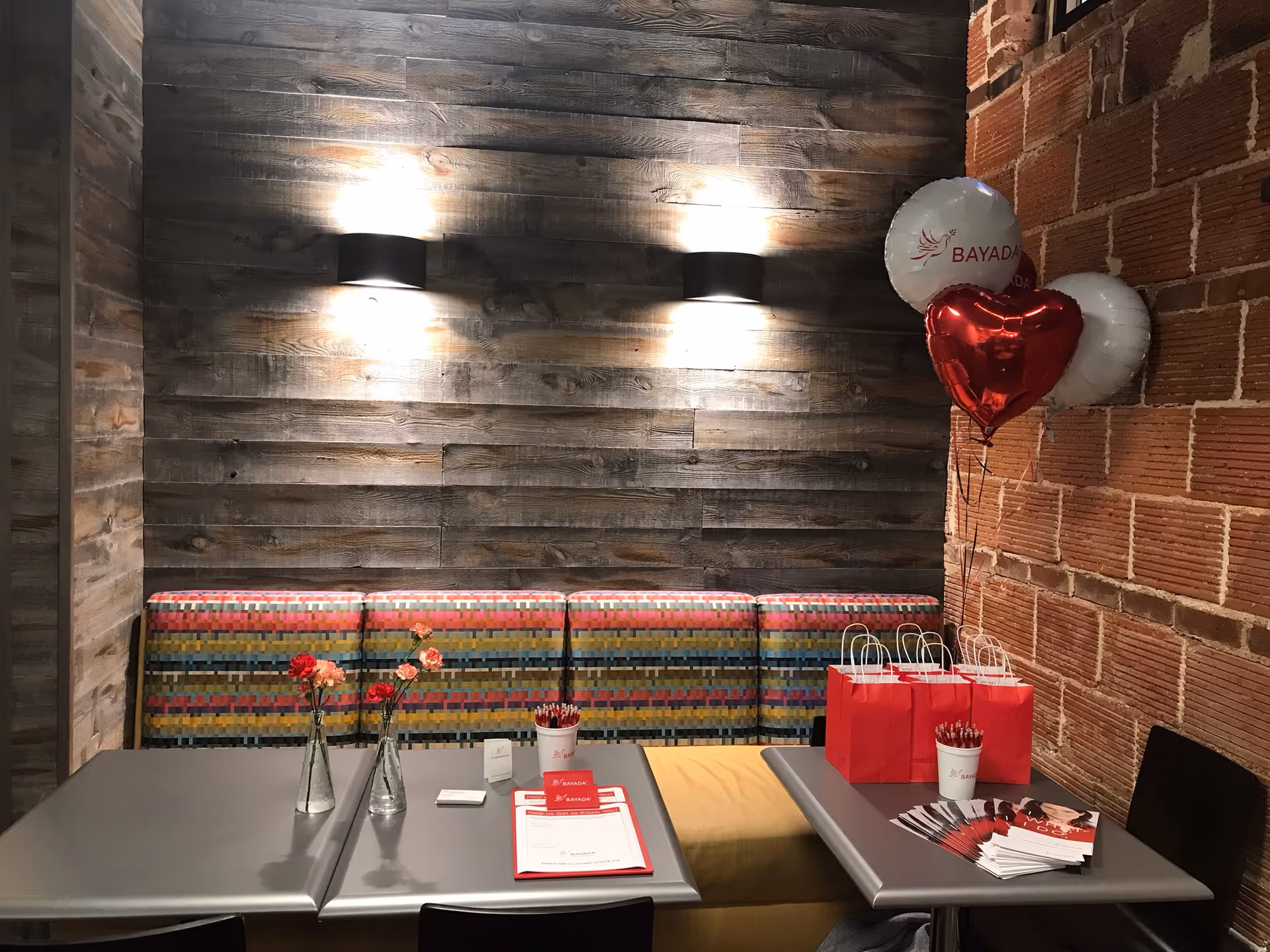 Indoor dining area with gray tables, colorful booth seating, balloons, and gift bags.