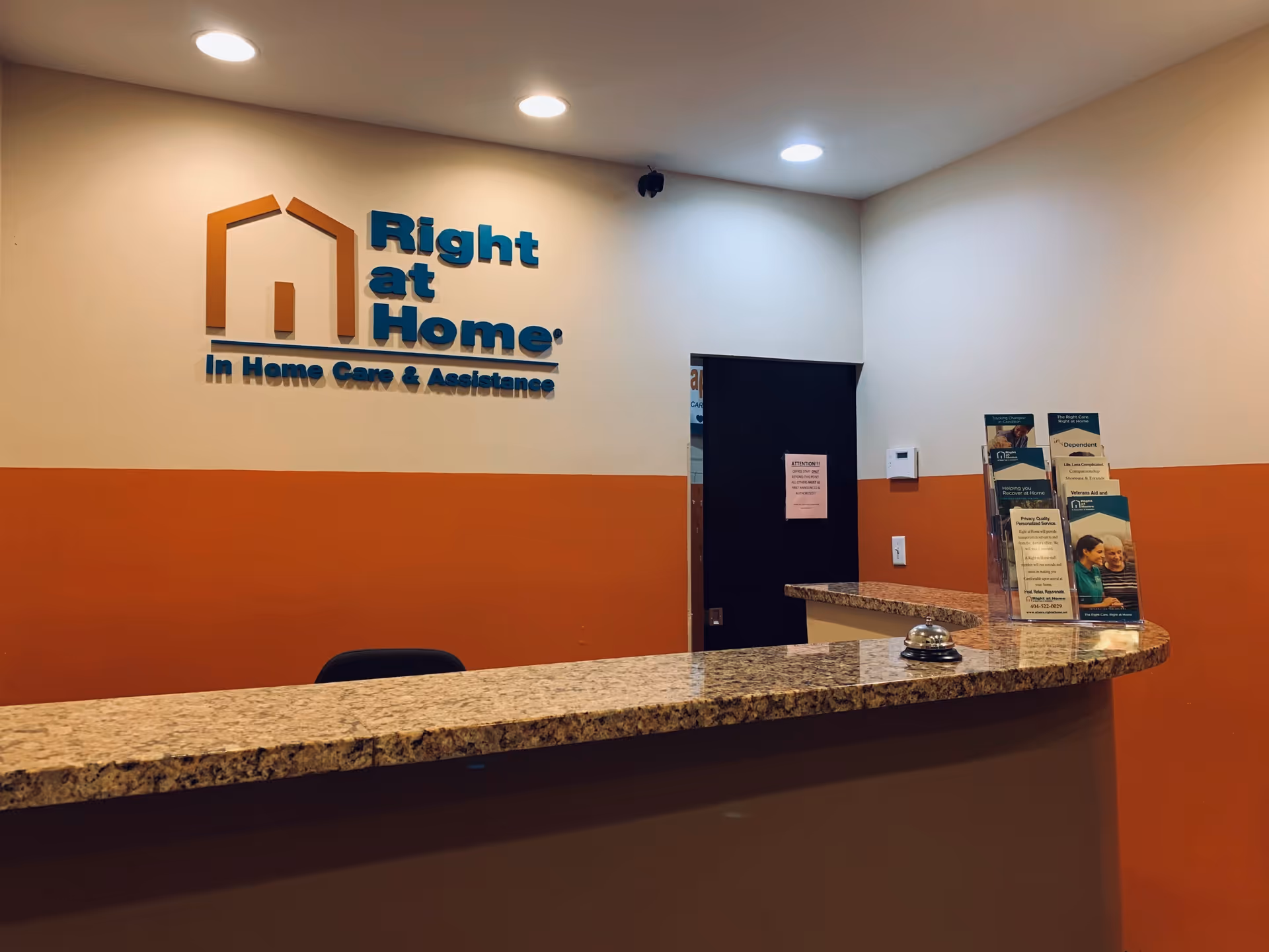 Reception desk with granite counter in Right at Home lobby; brochures and logo on wall