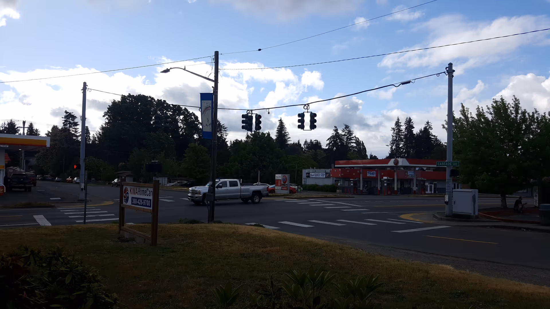 Wide street intersection with traffic lights and a distant red storefront, KWA Home Care sign nearby.