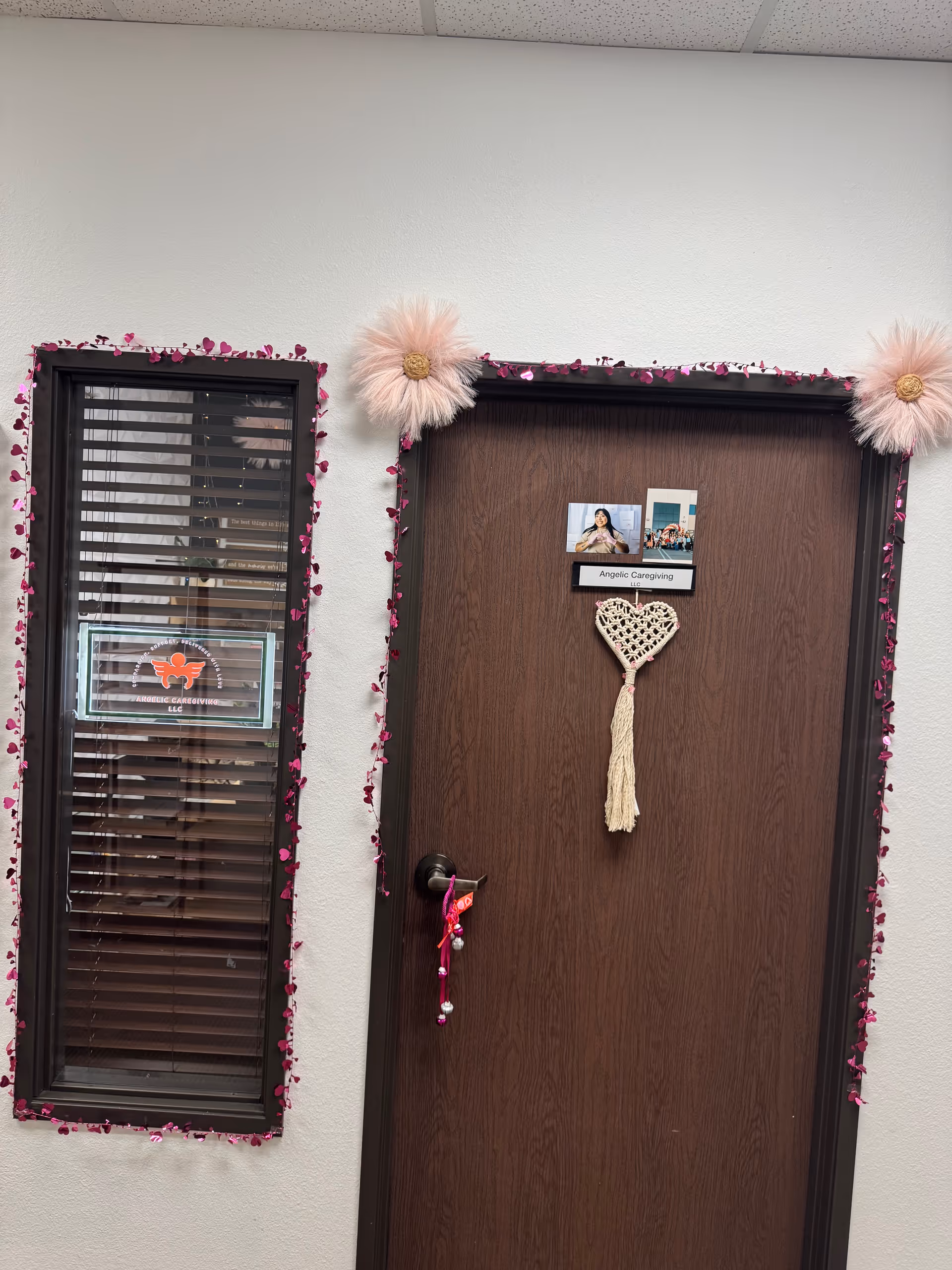 Wooden door labeled Angelic Caregiving LLC, decorated with pink garland and a heart tassel.