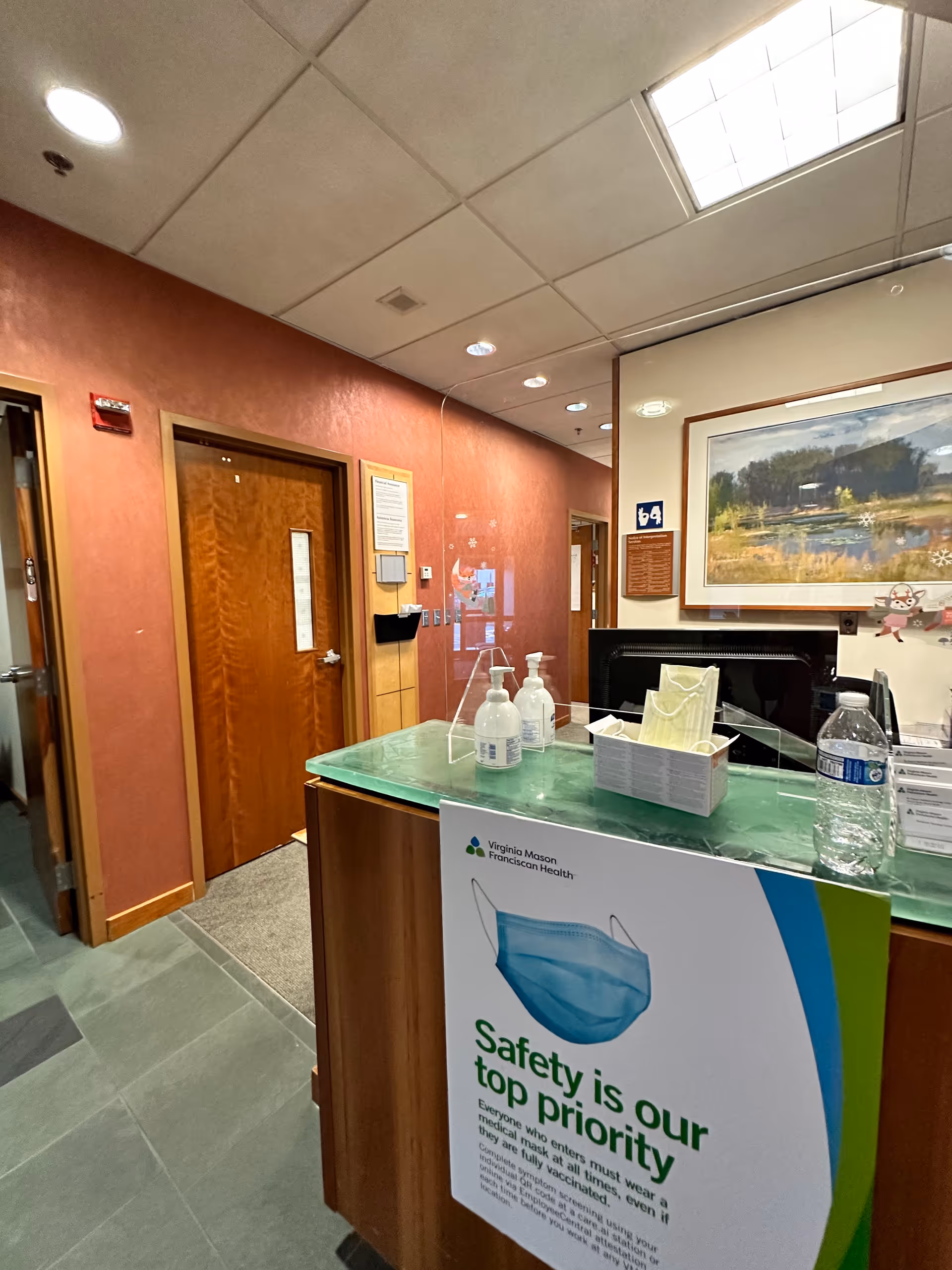 Interior hospital reception desk with sanitizer bottles and safety poster in a warm lobby.