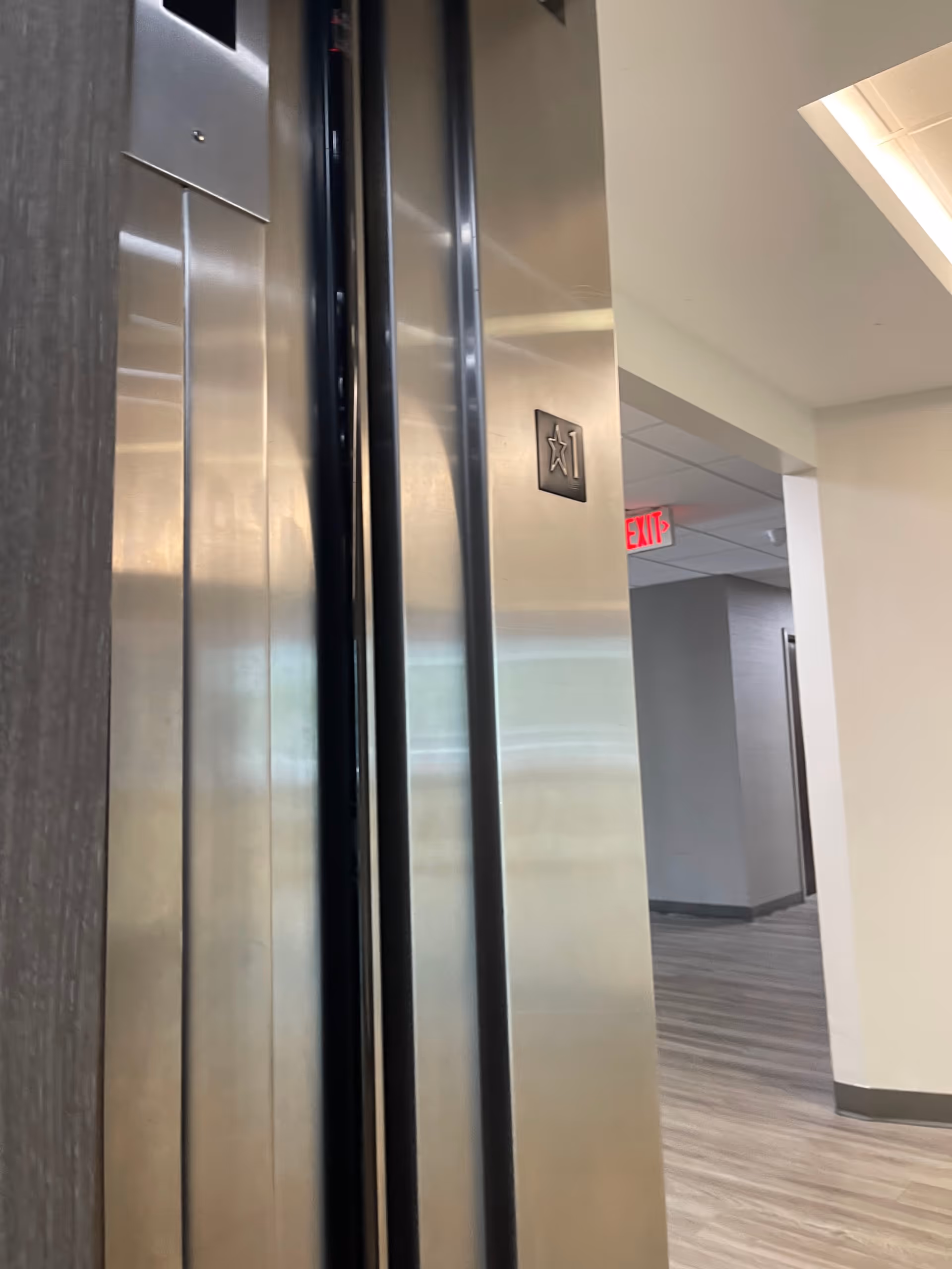 Elevator doors with surrounding hallway and exit sign in a modern interior.